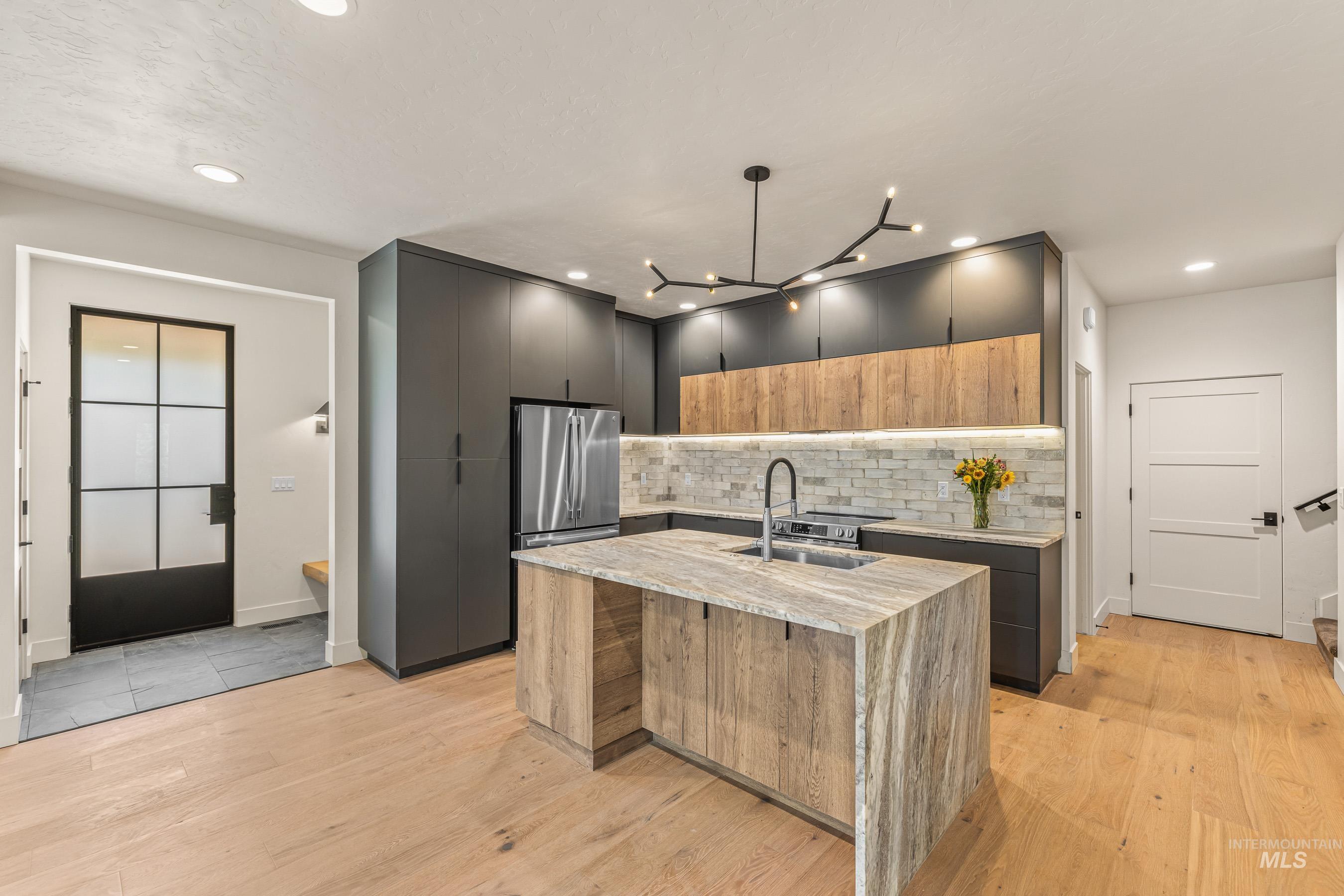Kitchen featuring light stone counters, two tone cabinets, modern cabinets, a kitchen island with sink, and stainless steel appliances