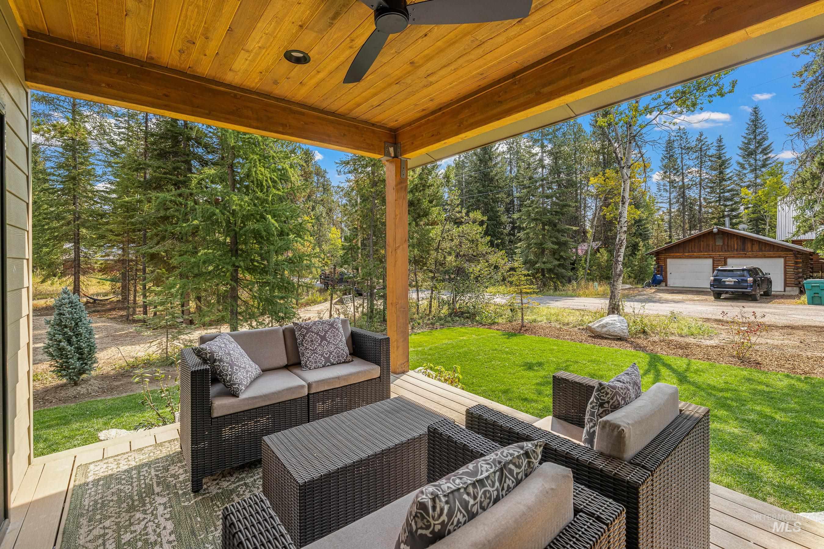 View of patio / terrace featuring outdoor seating, a detached garage, view of scattered trees, ceiling fan, and an outbuilding