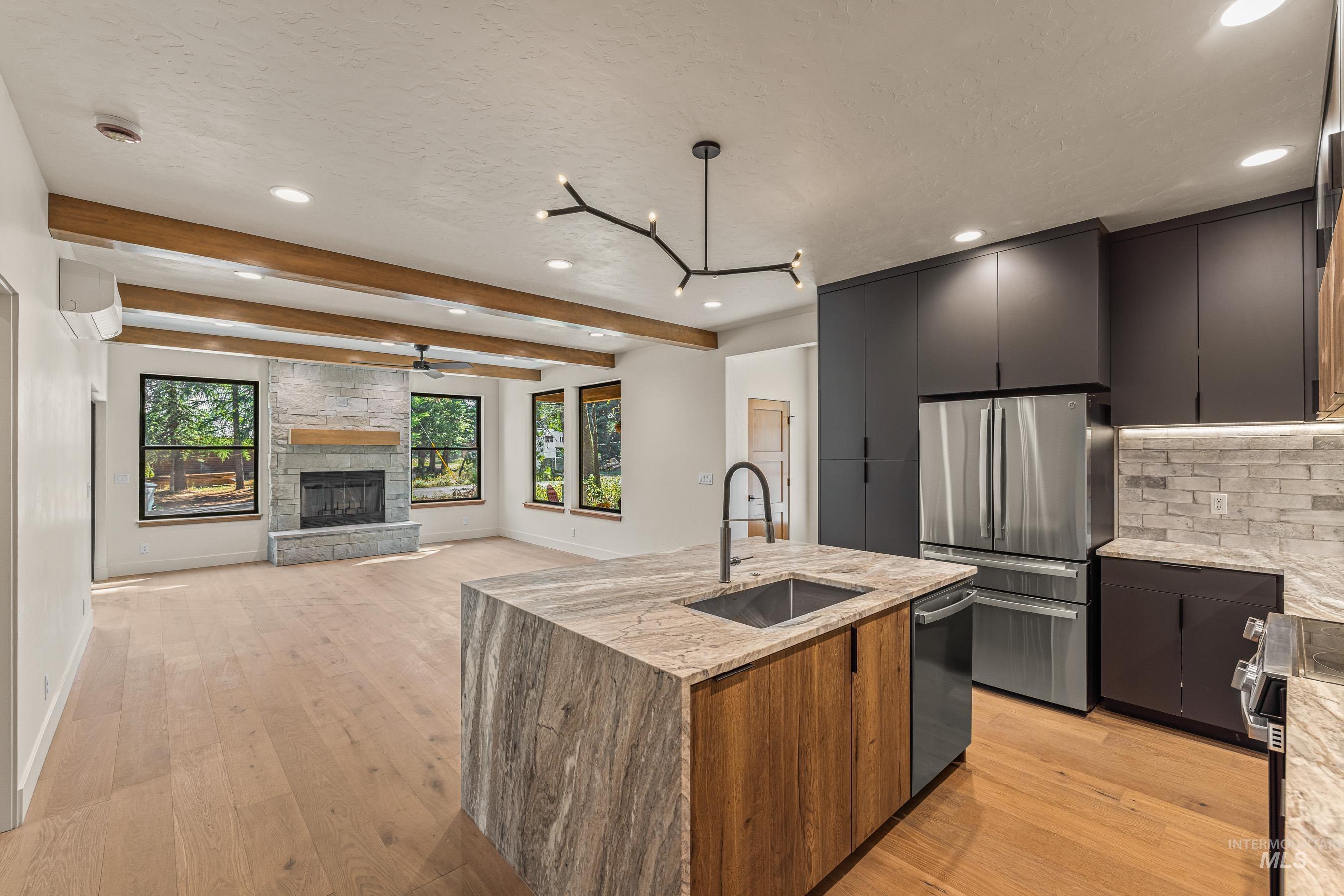 Kitchen with a stone fireplace, stainless steel appliances, open floor plan, light stone counters, and modern cabinets