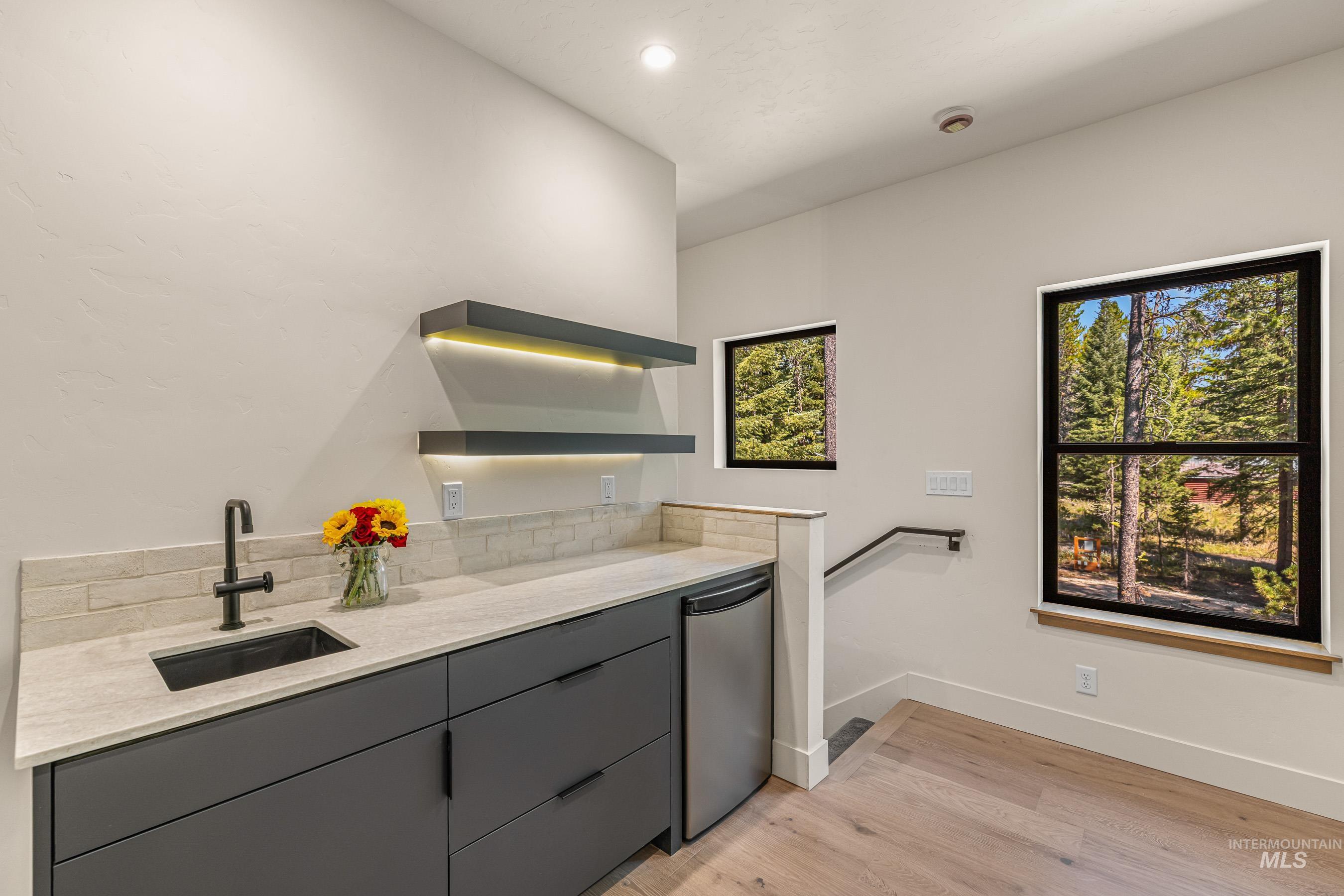 Kitchen featuring gray cabinetry, light stone counters, light wood-type flooring, open shelves, and stainless steel dishwasher