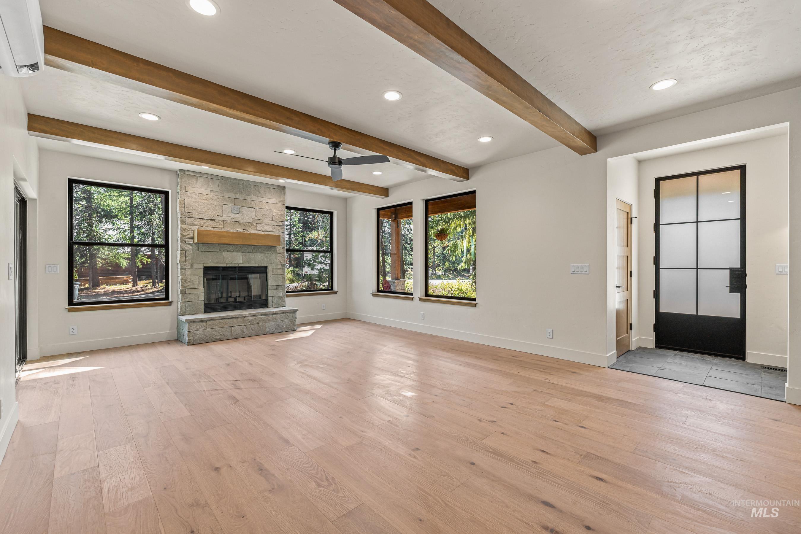 Unfurnished living room featuring light wood-type flooring, recessed lighting, a stone fireplace, a ceiling fan, and beamed ceiling