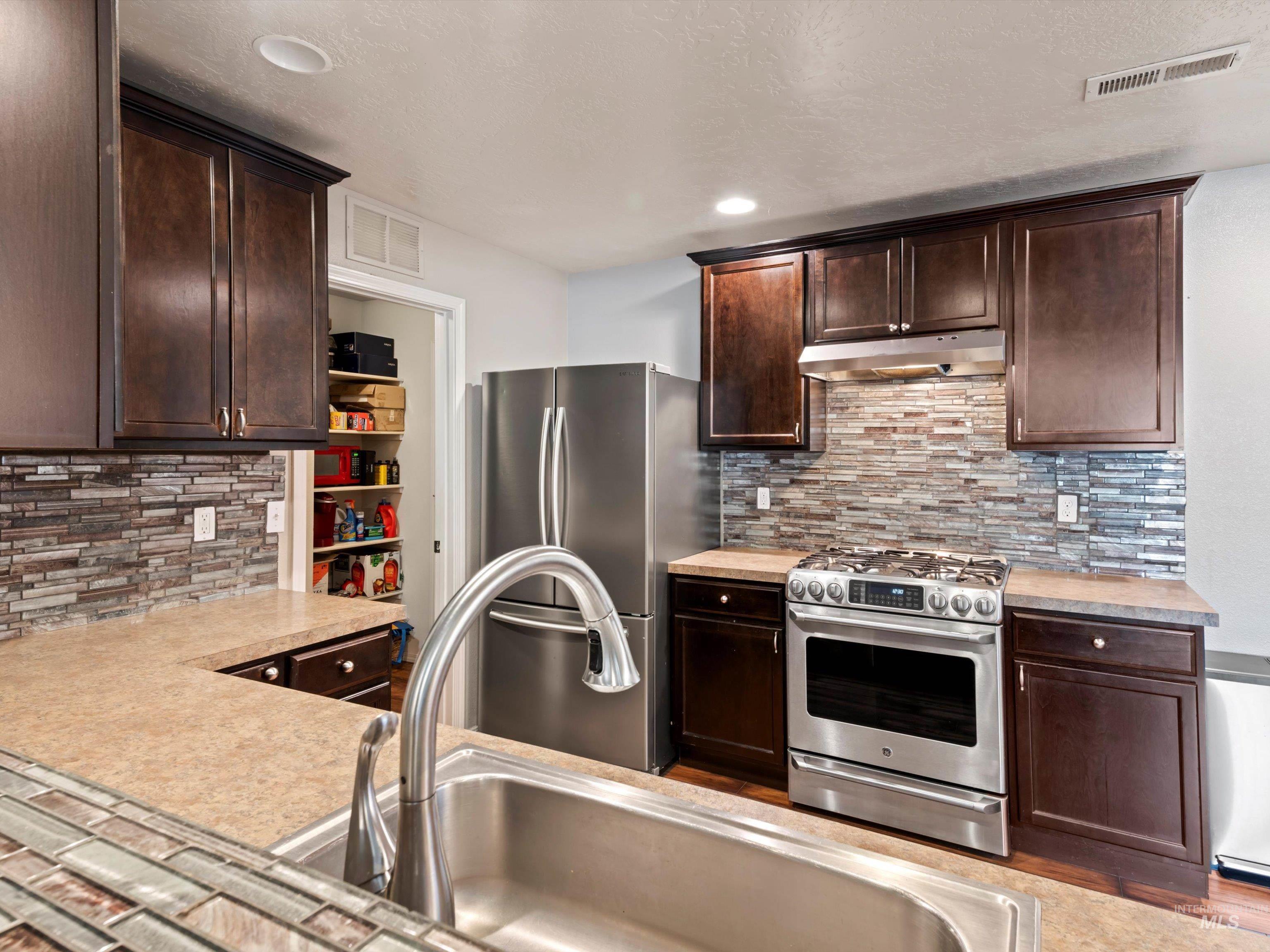 Kitchen featuring dark brown cabinets, stainless steel appliances, light countertops, a textured ceiling, and recessed lighting