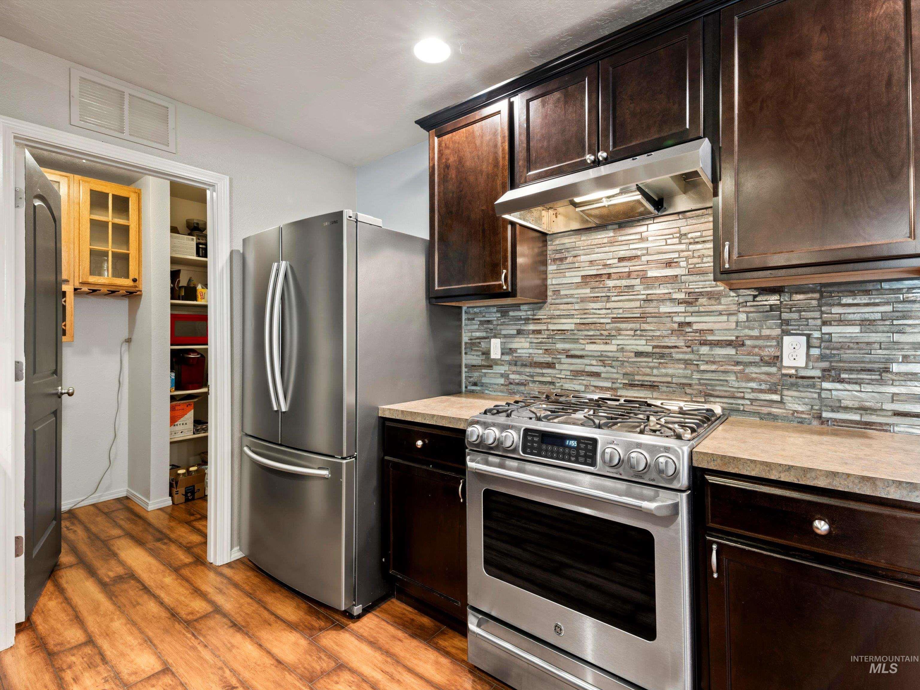 Kitchen with stainless steel appliances, light countertops, tasteful backsplash, under cabinet range hood, and dark brown cabinets