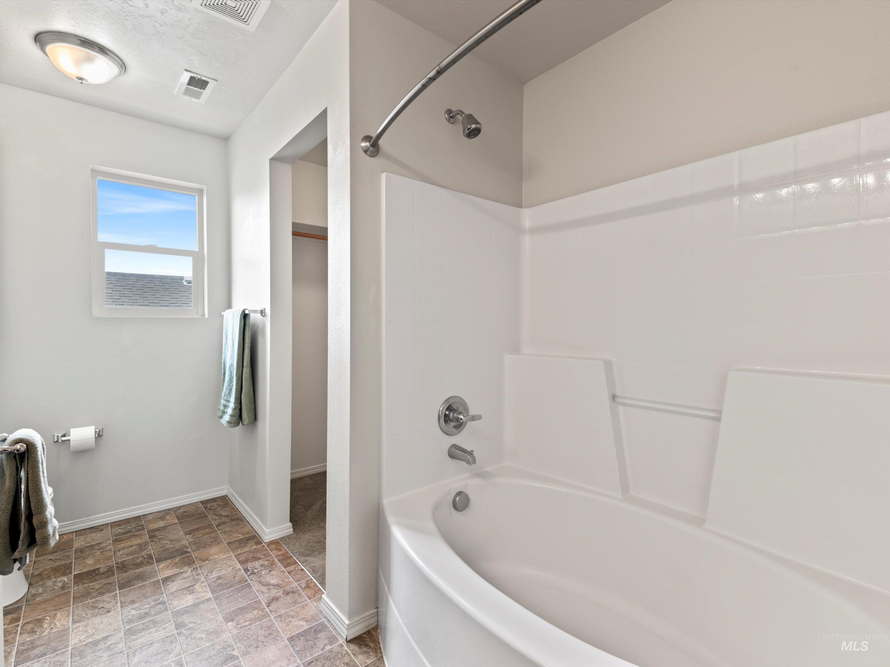 Bathroom featuring bathtub / shower combination and stone finish flooring
