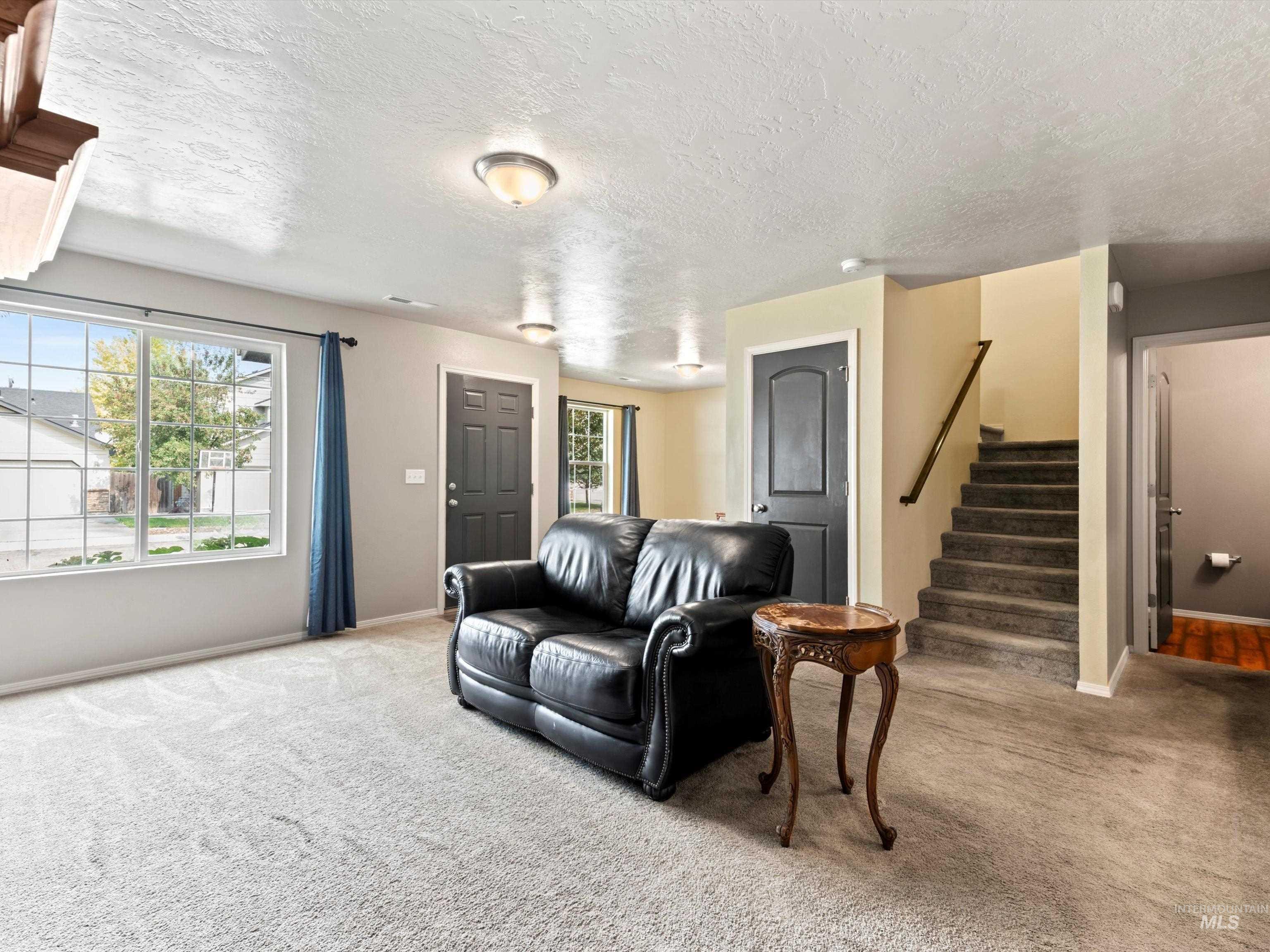Living room featuring plenty of natural light, stairway, carpet flooring, and a textured ceiling