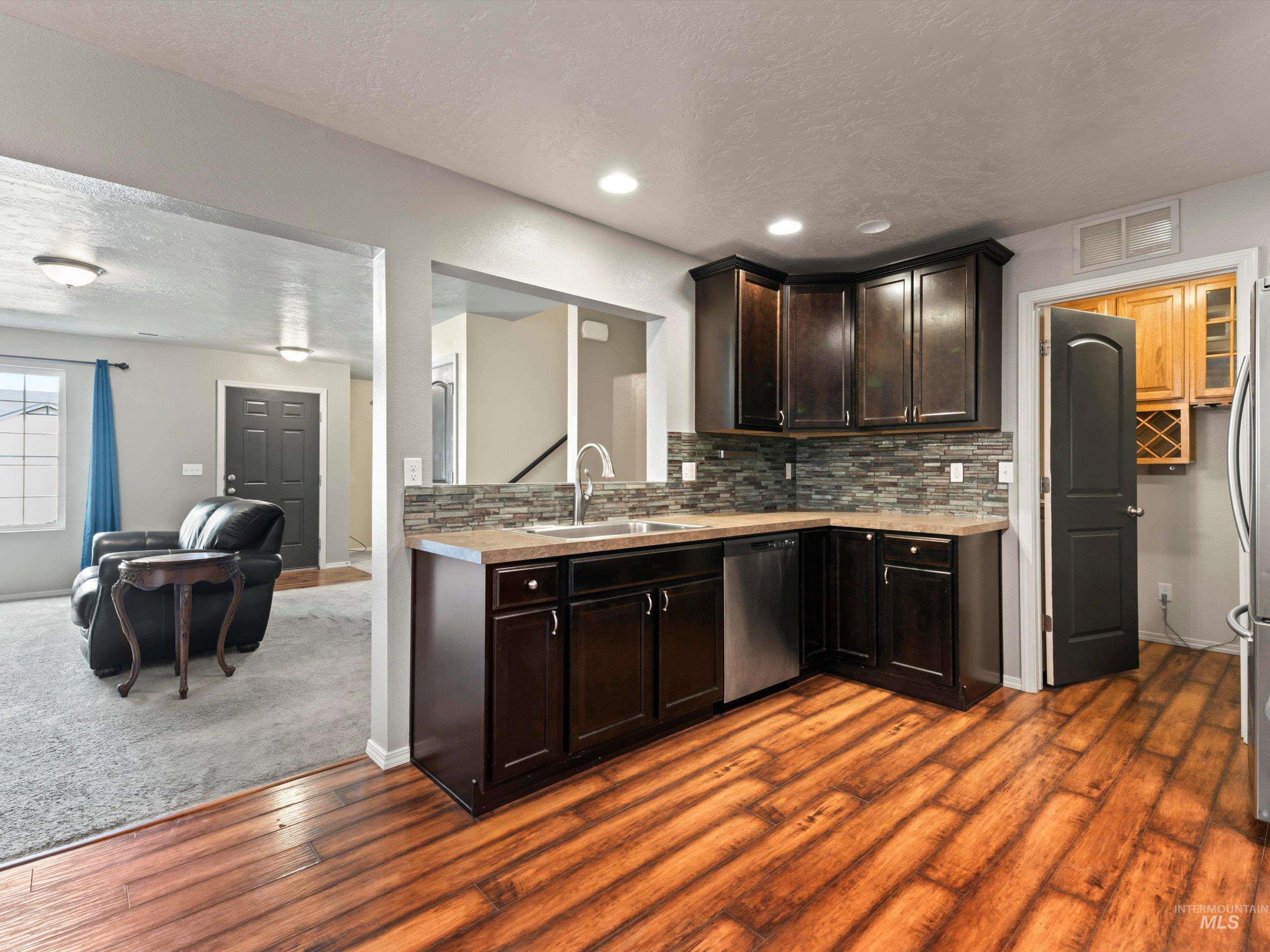 Kitchen with a textured ceiling, decorative backsplash, open floor plan, dark brown cabinets, and dark wood-style flooring