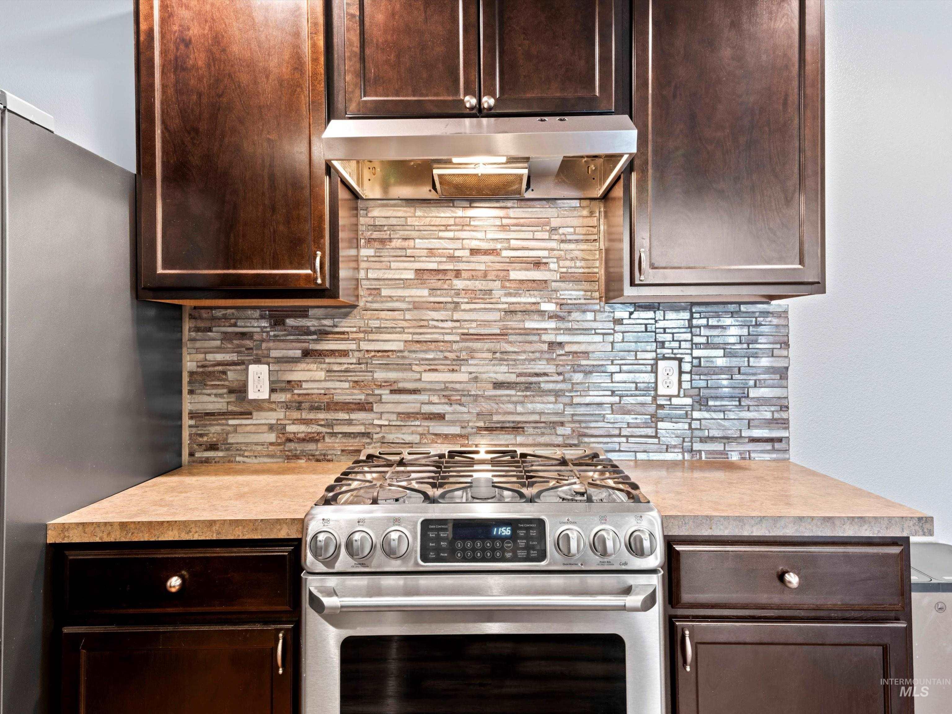 Kitchen featuring stainless steel appliances, dark brown cabinetry, tasteful backsplash, light countertops, and under cabinet range hood