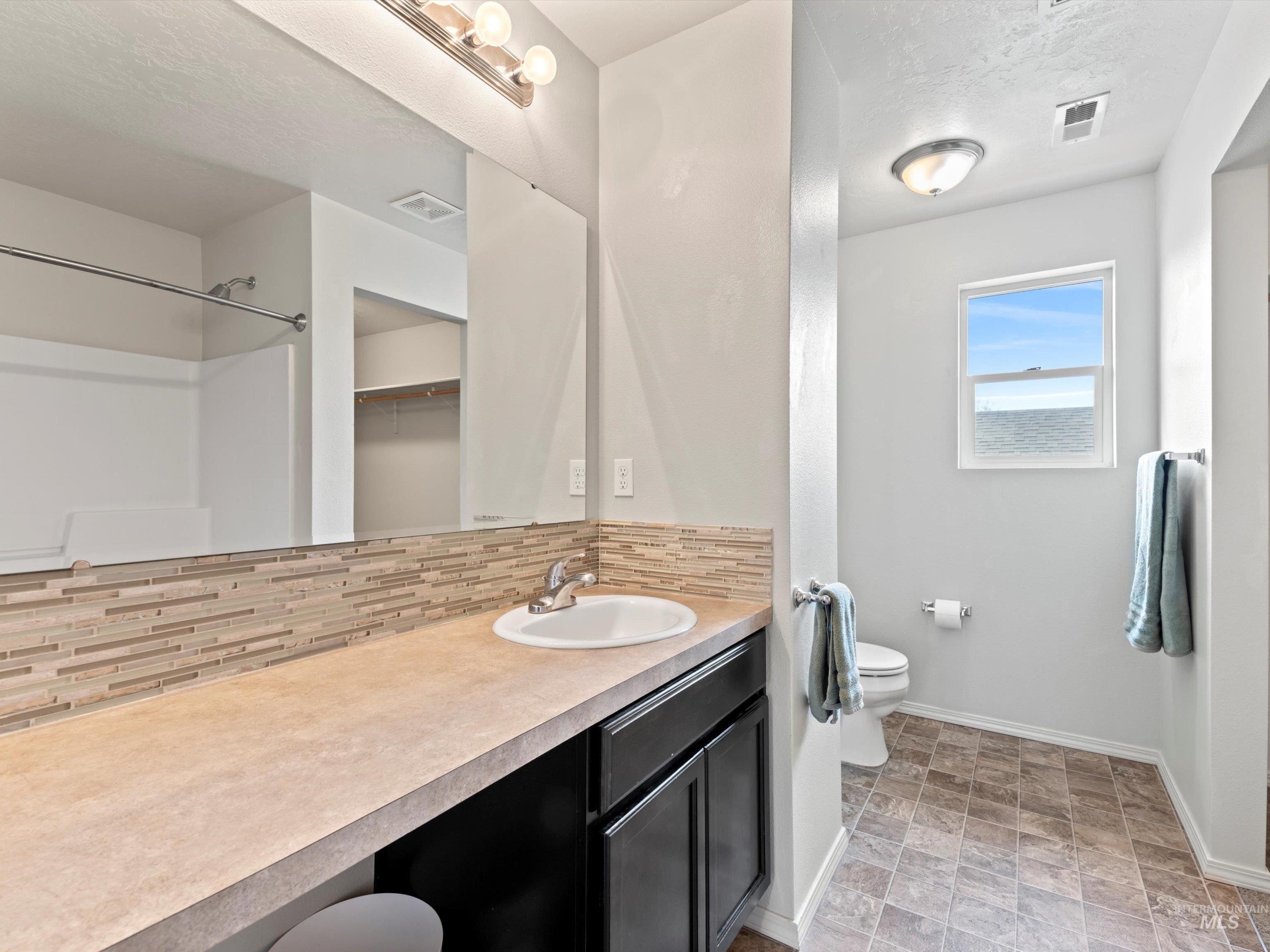 Bathroom with vanity, backsplash, a spacious closet, stone finish floors, and a textured ceiling