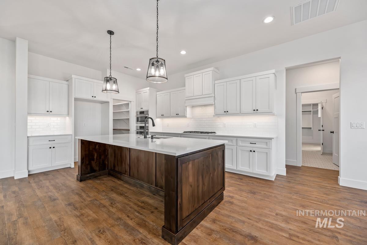 Kitchen featuring white cabinets, dark brown cabinets, a kitchen island with sink, pendant lighting, and recessed lighting