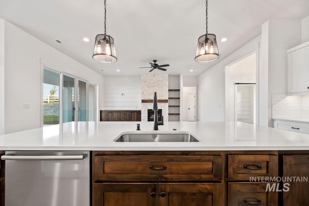 Kitchen featuring dishwasher, dark brown cabinets, hanging light fixtures, ceiling fan, and light stone countertops