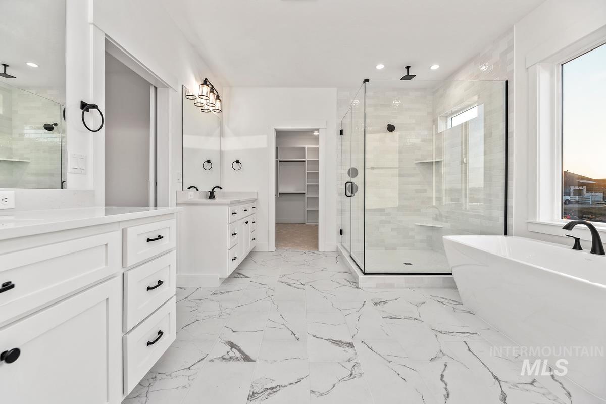 Bathroom featuring a spacious closet, a stall shower, a freestanding tub, two vanities, and recessed lighting