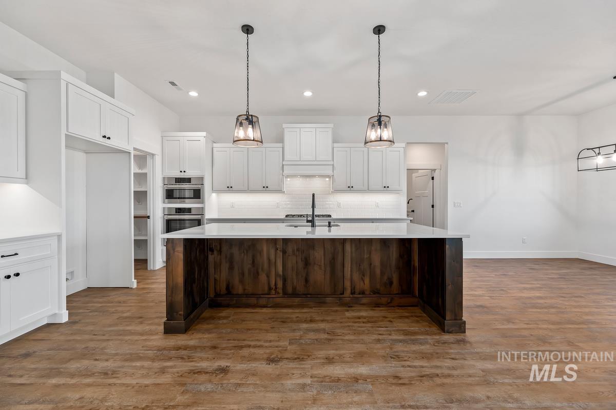 Kitchen with white cabinets, dark wood finished floors, decorative light fixtures, a center island with sink, and dark brown cabinetry