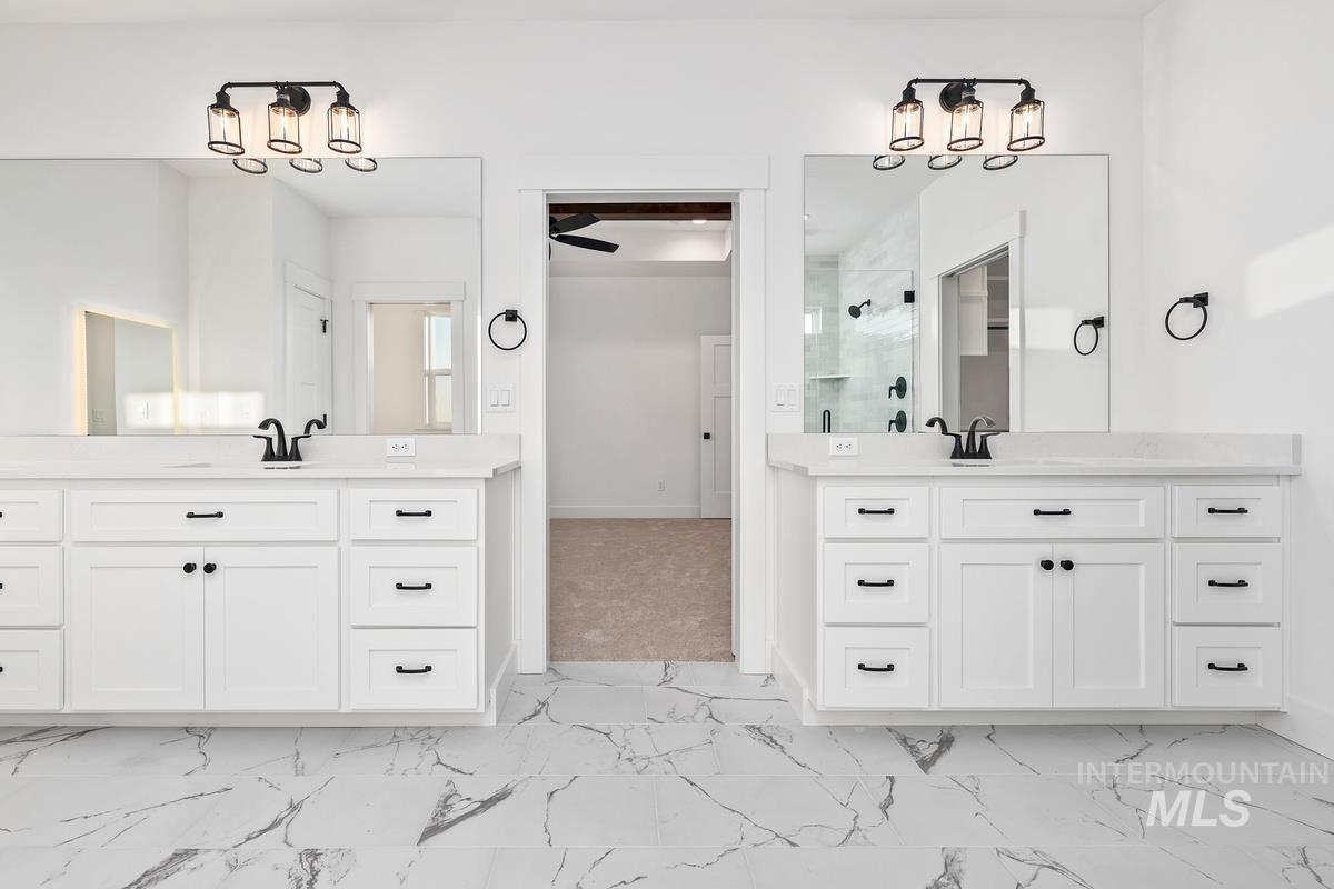 Full bath featuring light marble finish flooring, a shower stall, and two vanities