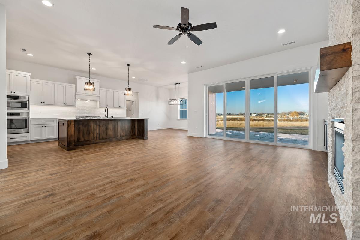 Unfurnished living room featuring a stone fireplace, dark wood-type flooring, a ceiling fan, a chandelier, and recessed lighting