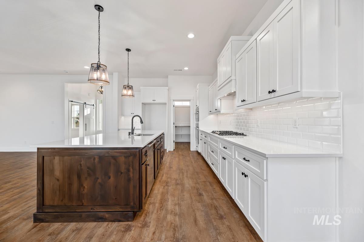 Kitchen with white cabinets, dark brown cabinetry, an island with sink, decorative light fixtures, and recessed lighting