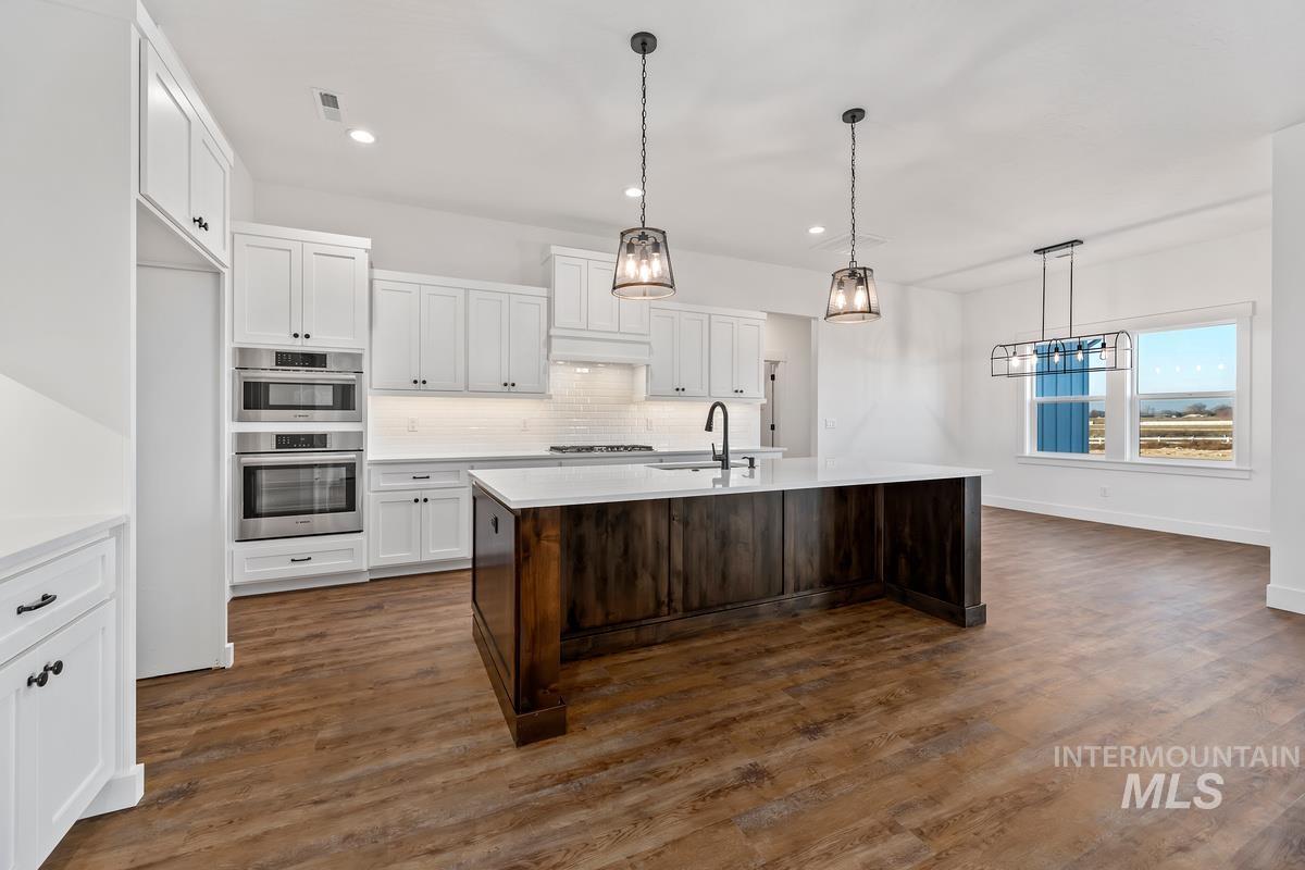 Kitchen with white cabinets, hanging light fixtures, dark brown cabinets, a center island with sink, and dark wood-style floors