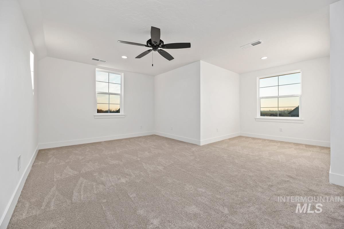Empty room with light colored carpet, healthy amount of natural light, and ceiling fan