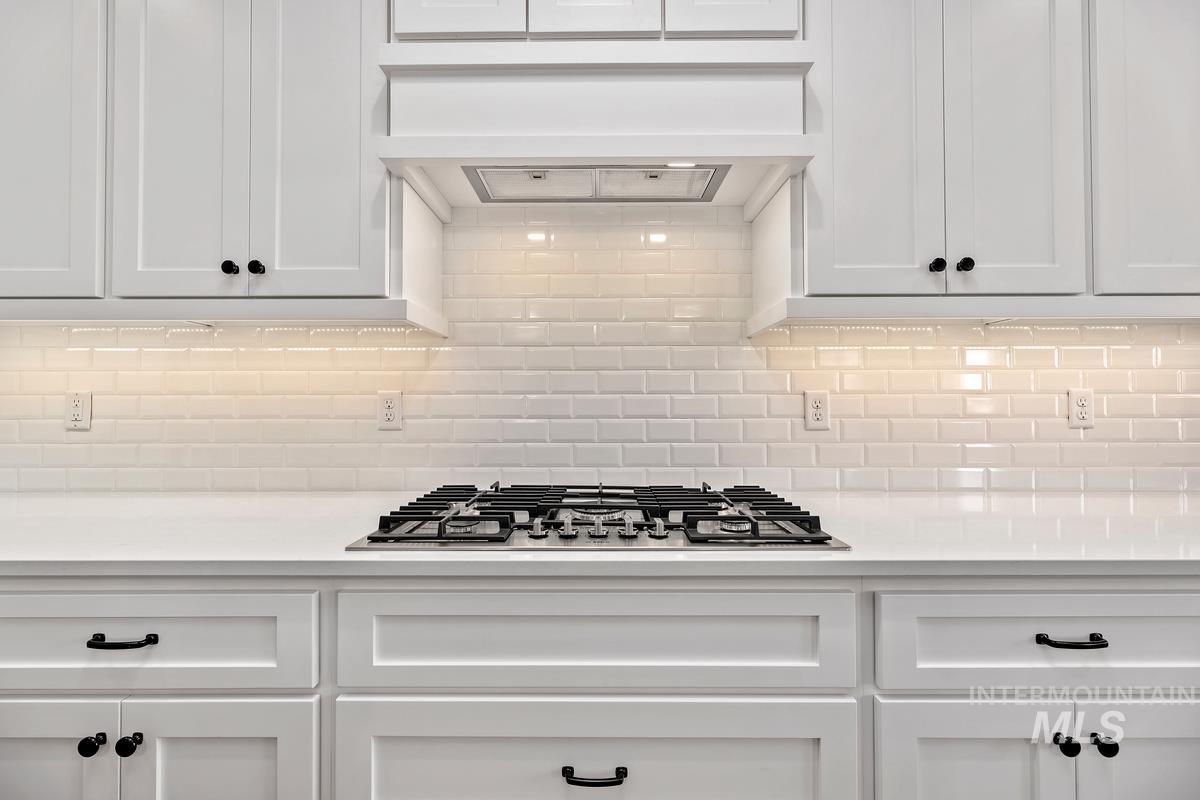 Kitchen featuring white cabinetry, premium range hood, stainless steel gas cooktop, and light stone counters