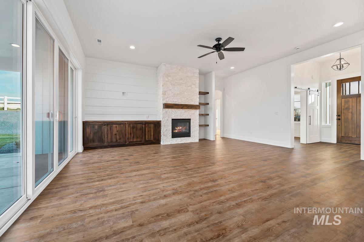 Unfurnished living room featuring a barn door, wood finished floors, a ceiling fan, a stone fireplace, and recessed lighting