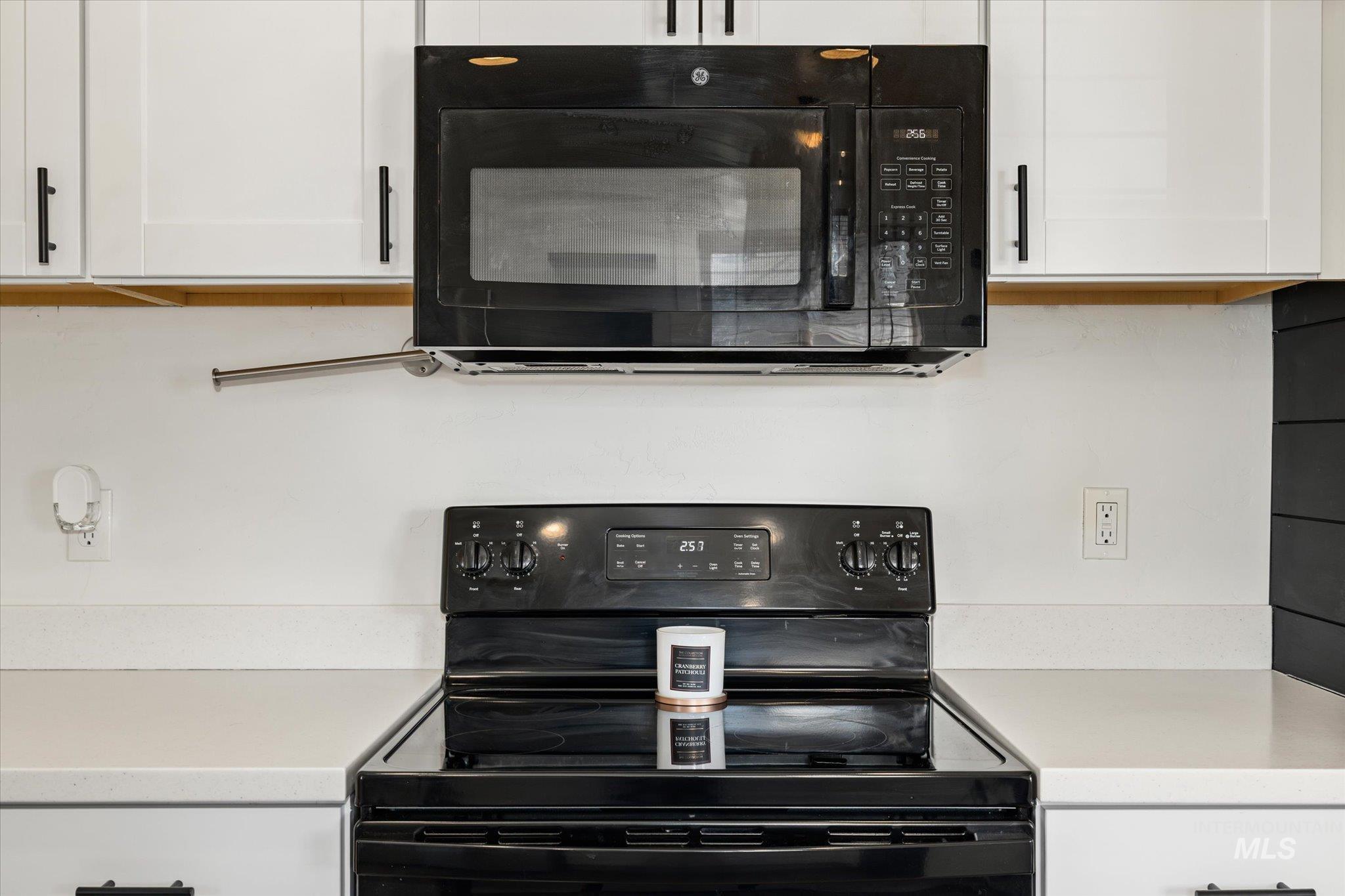 Kitchen view of black appliances, white cabinetry, and light stone counters