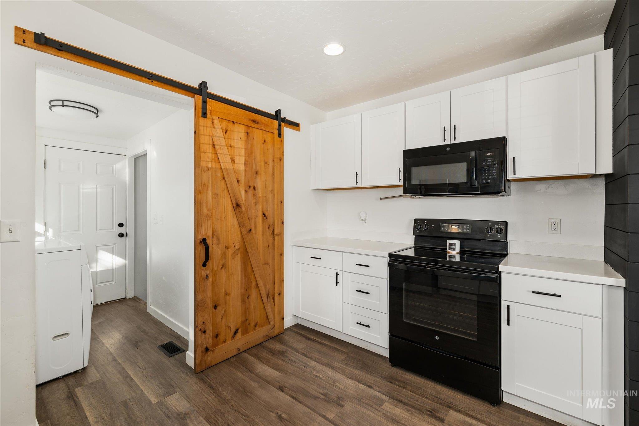 Kitchen with a barn door, black appliances, white cabinets, light countertops, and recessed lighting