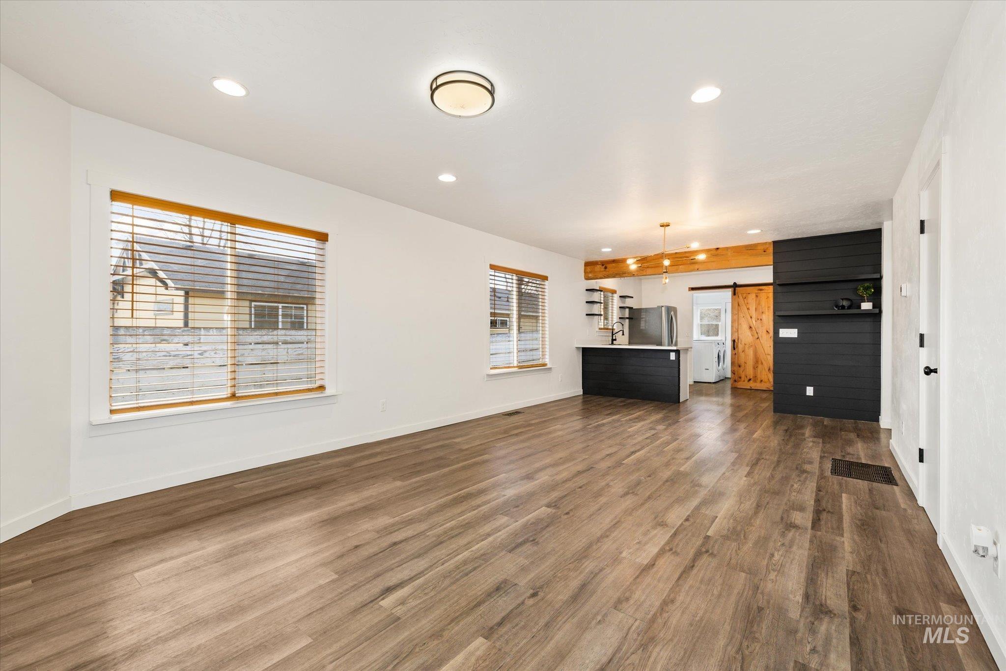 Unfurnished living room featuring a barn door, plenty of natural light, recessed lighting, and dark wood finished floors