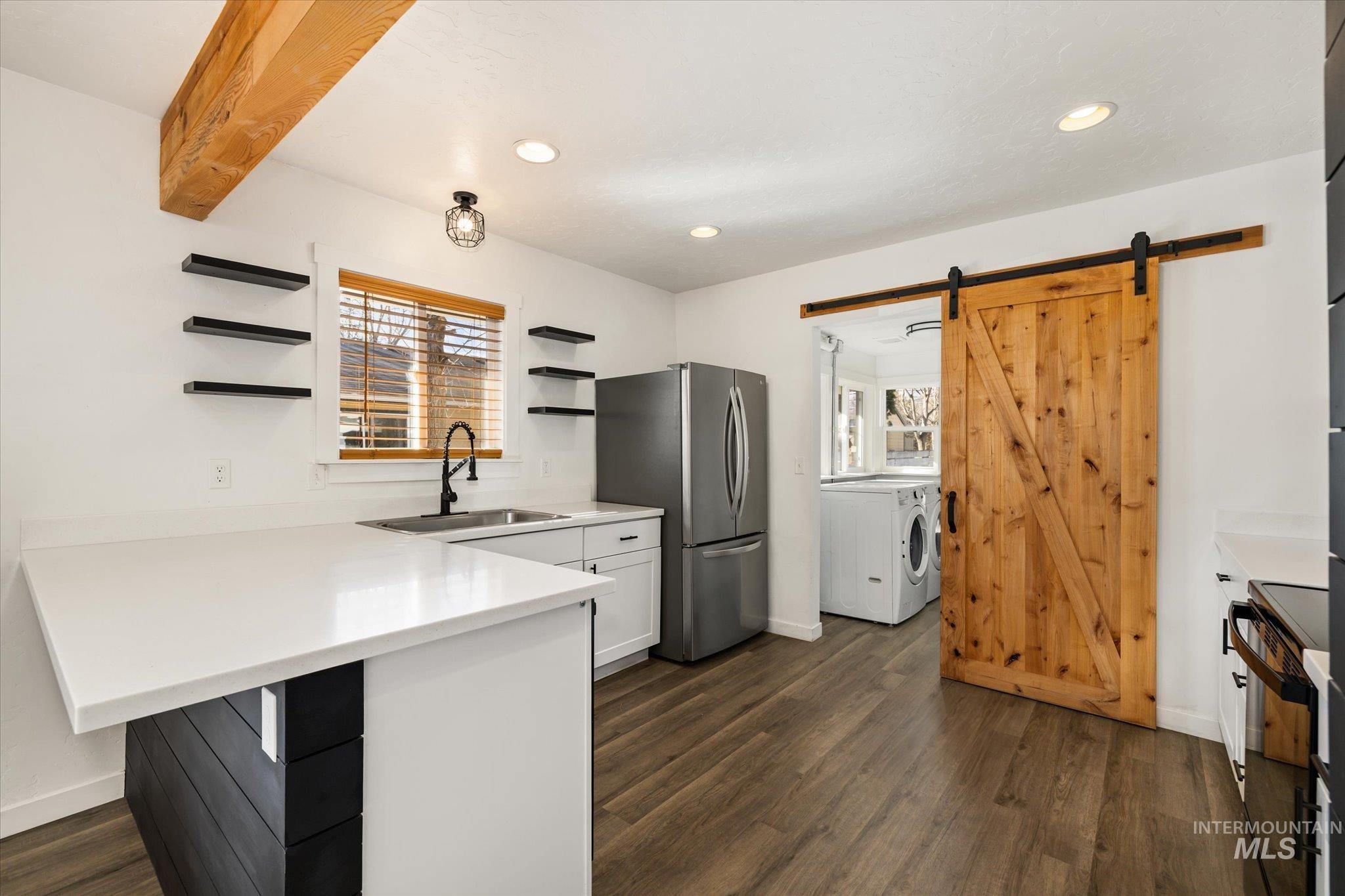 Kitchen featuring a barn door, open shelves, light countertops, freestanding refrigerator, and a peninsula