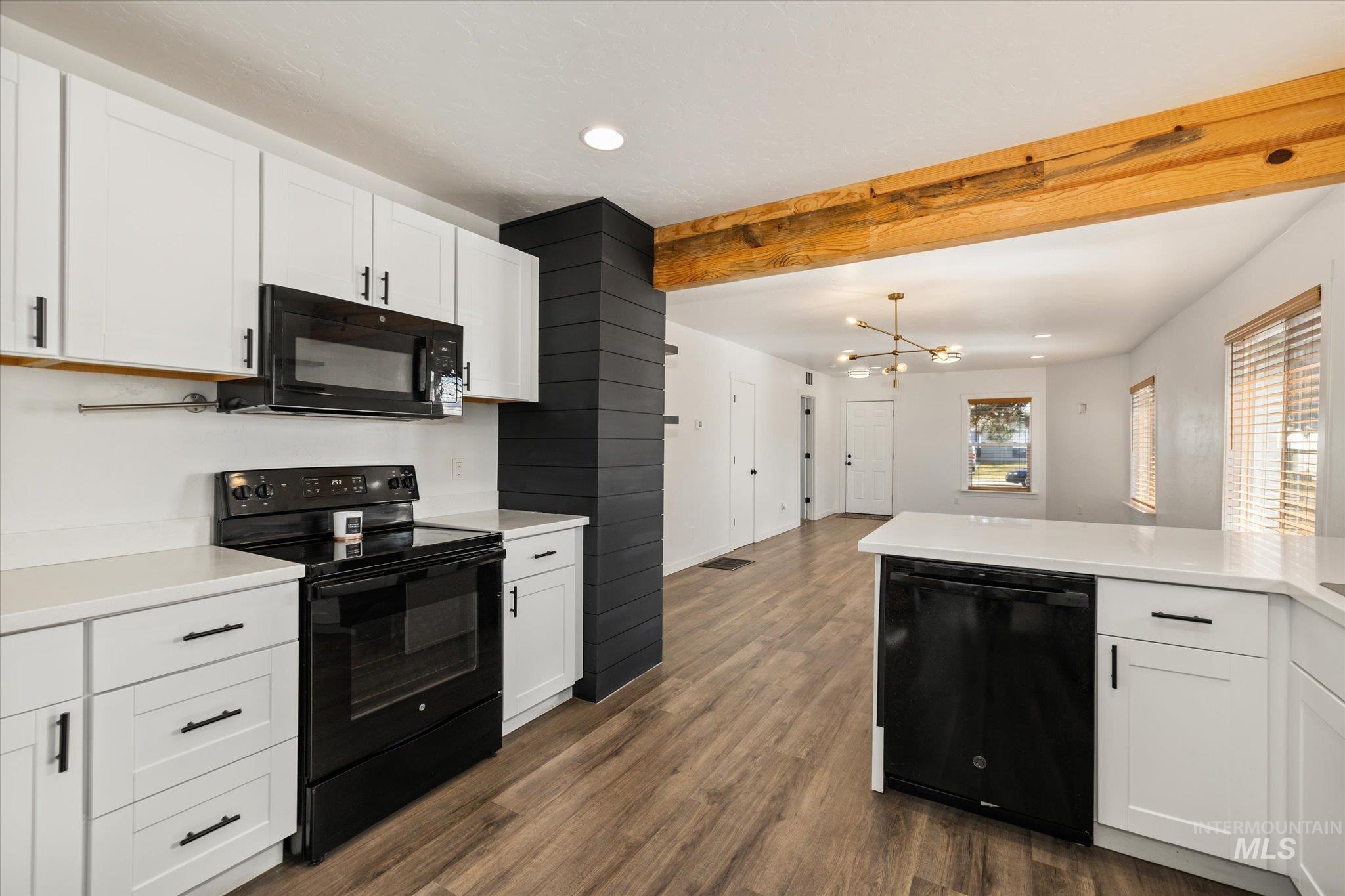 Kitchen with white cabinetry, black appliances, a chandelier, dark wood finished floors, and beam ceiling