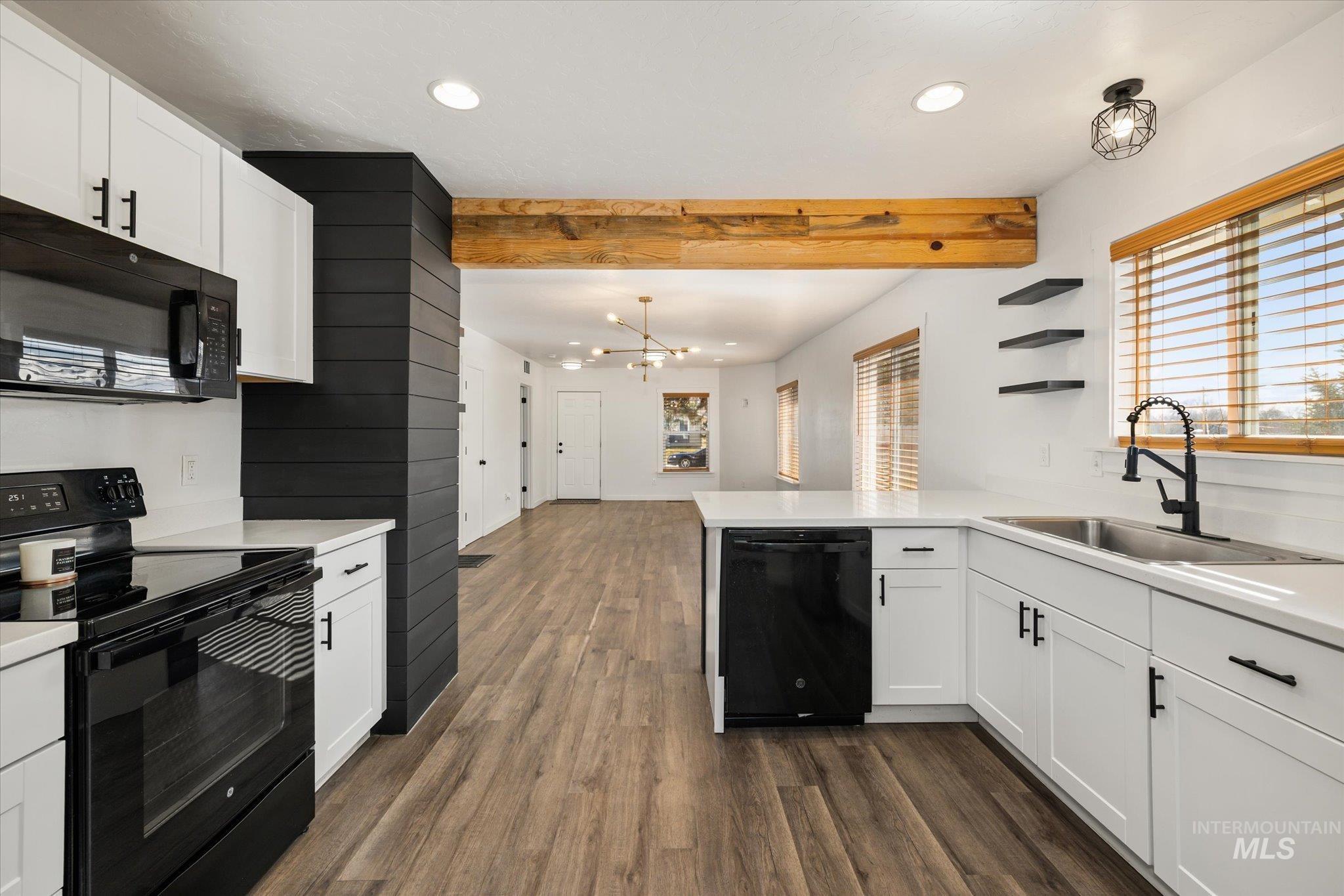 Kitchen featuring black appliances, white cabinetry, a peninsula, dark wood finished floors, and a chandelier