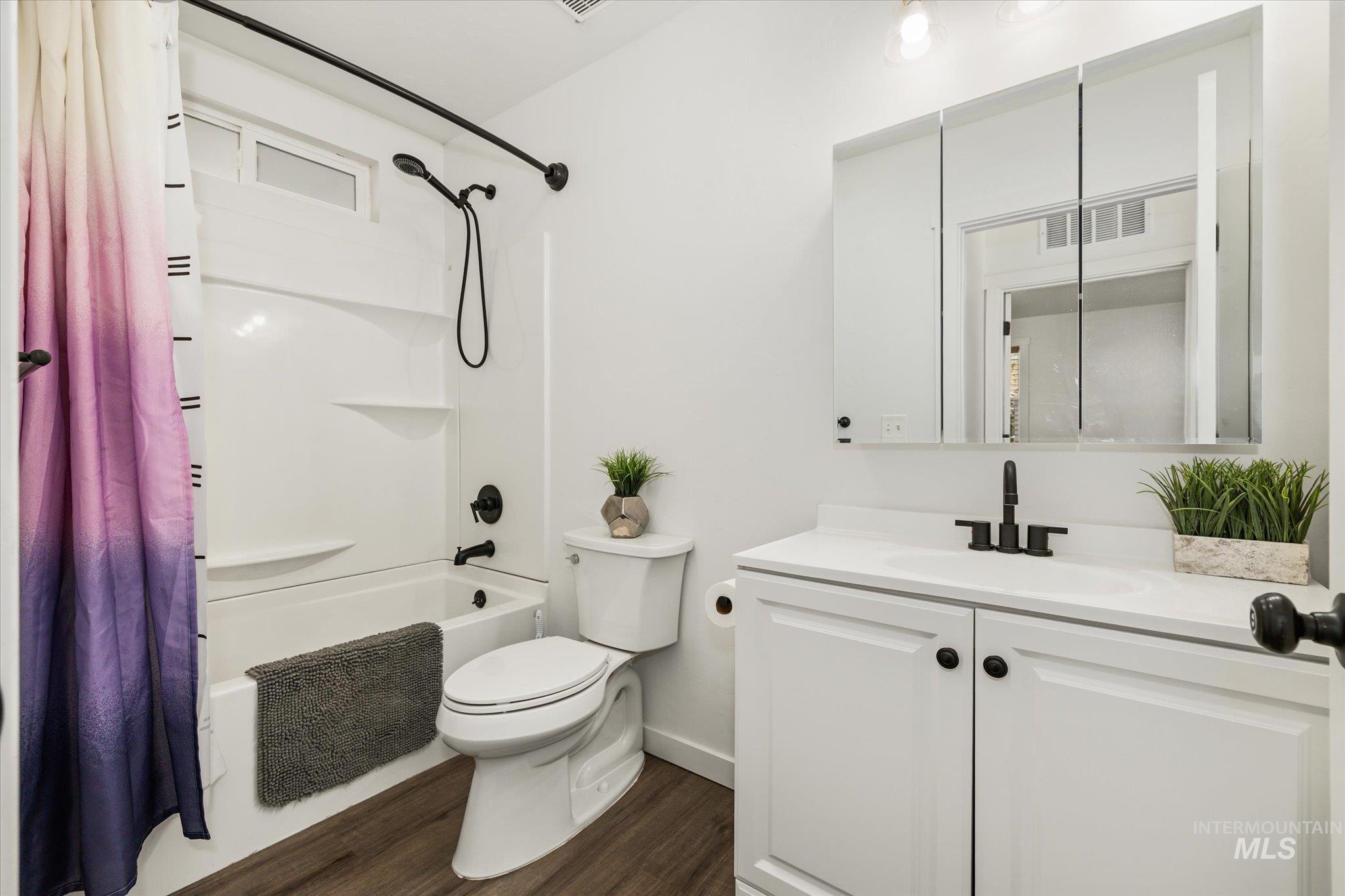 Full bathroom featuring shower / bath combo with shower curtain, vanity, and dark wood-type flooring