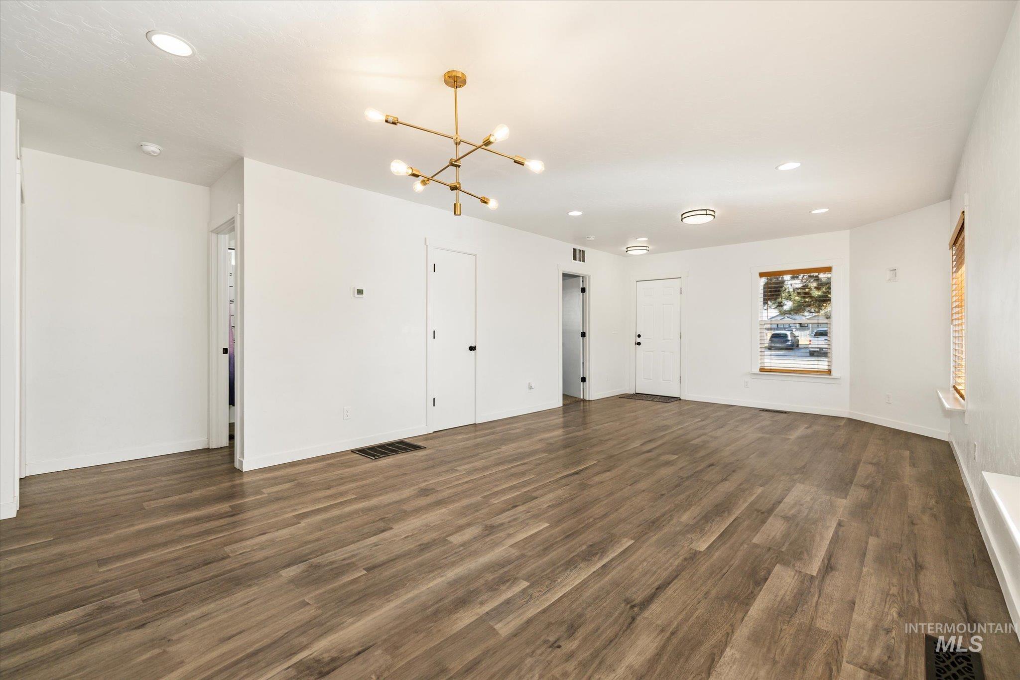 Unfurnished living room featuring a chandelier and dark wood-style floors