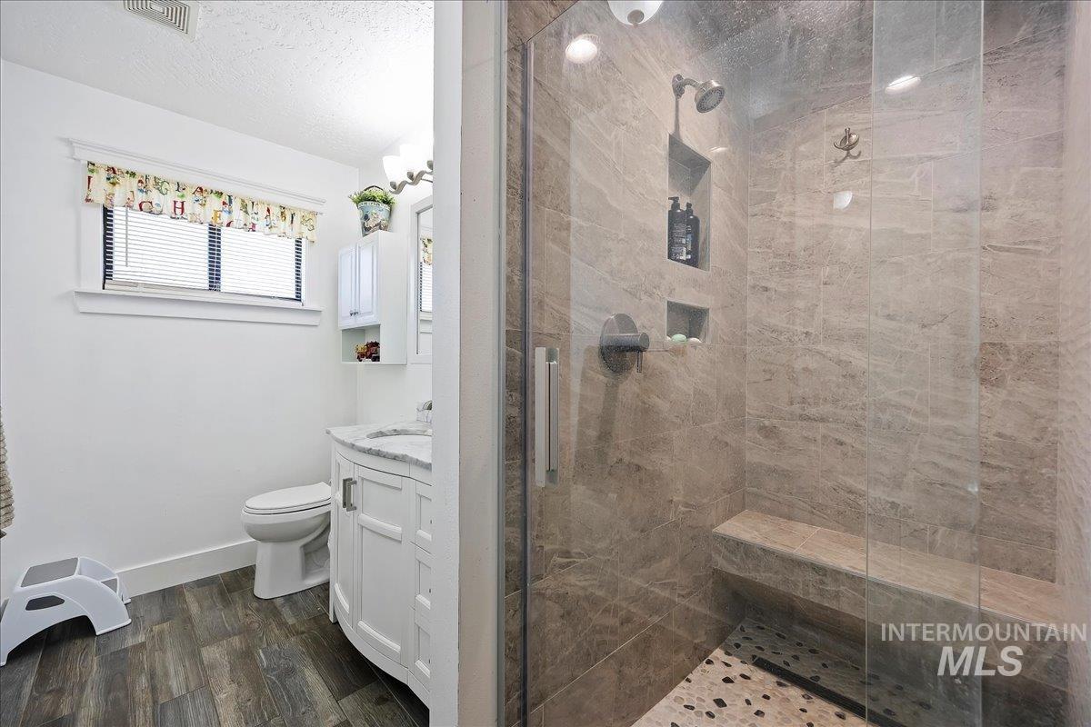 Full bath with vanity, a stall shower, a textured ceiling, and dark wood-style flooring