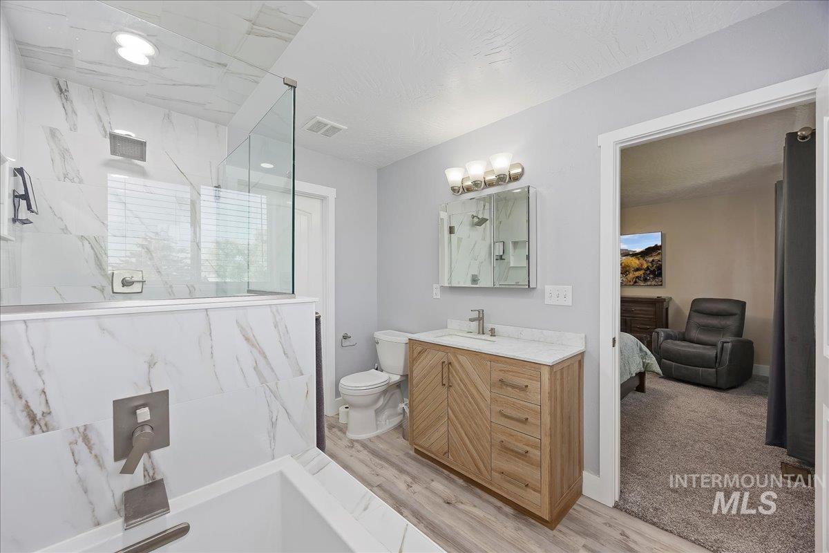 Ensuite bathroom featuring vanity, a marble finish shower, and light wood-style flooring