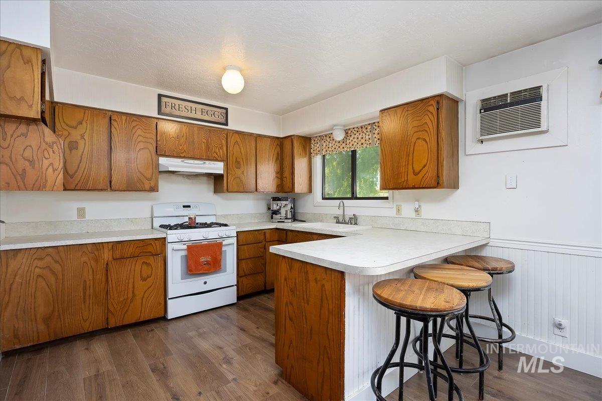 Kitchen with brown cabinetry, a breakfast bar, white range with gas cooktop, a peninsula, and light countertops
