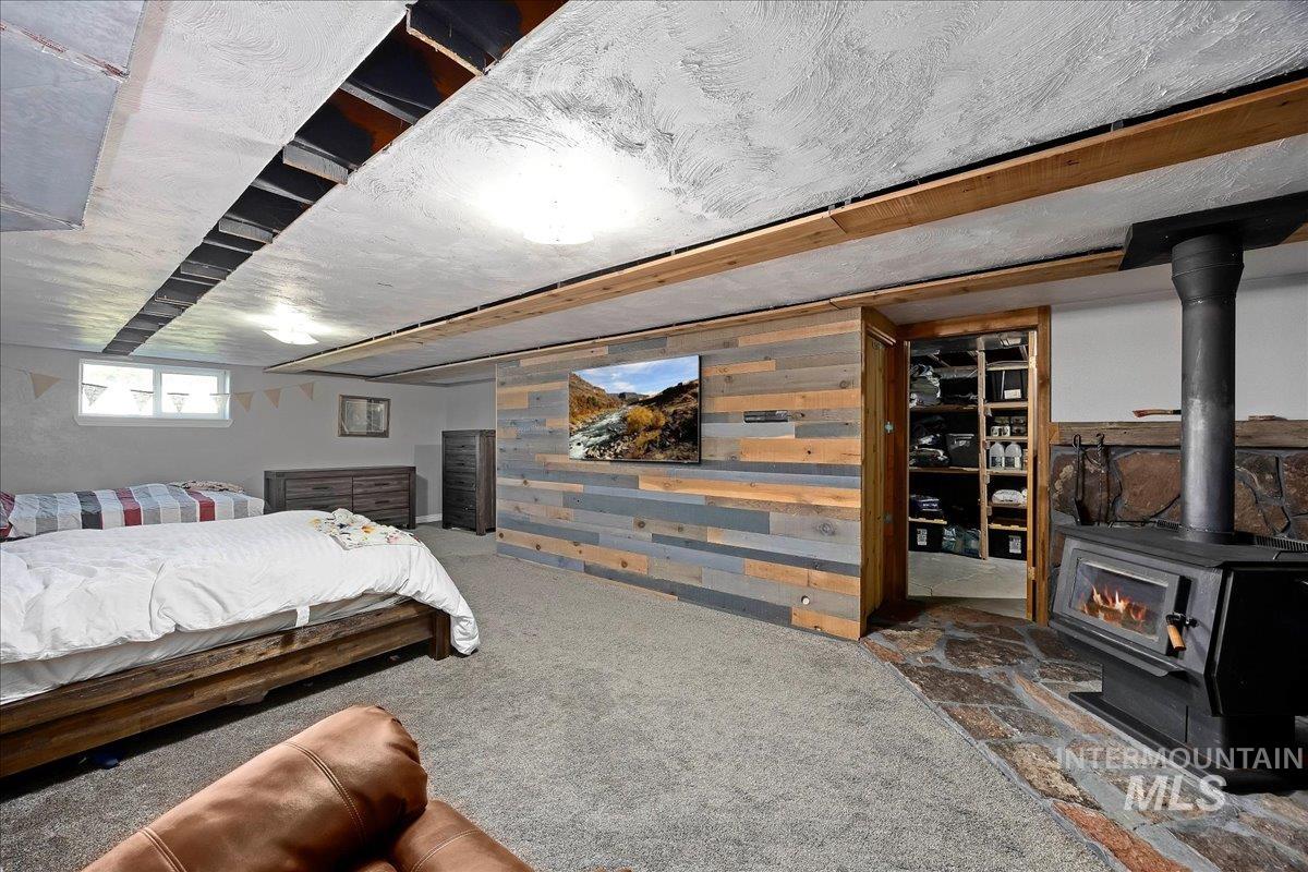 Bedroom with wooden walls, carpet floors, and a wood stove