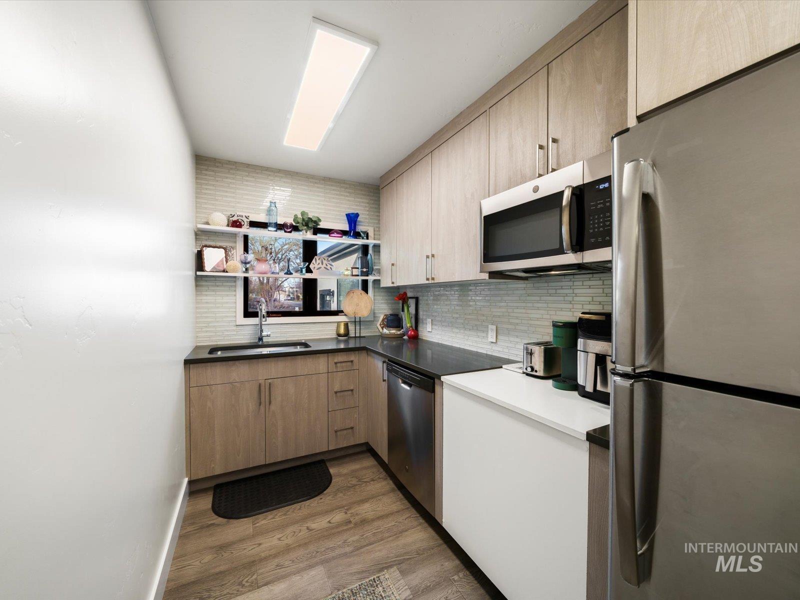 Kitchen with stainless steel appliances, open shelves, dark countertops, light wood-style flooring, and backsplash
