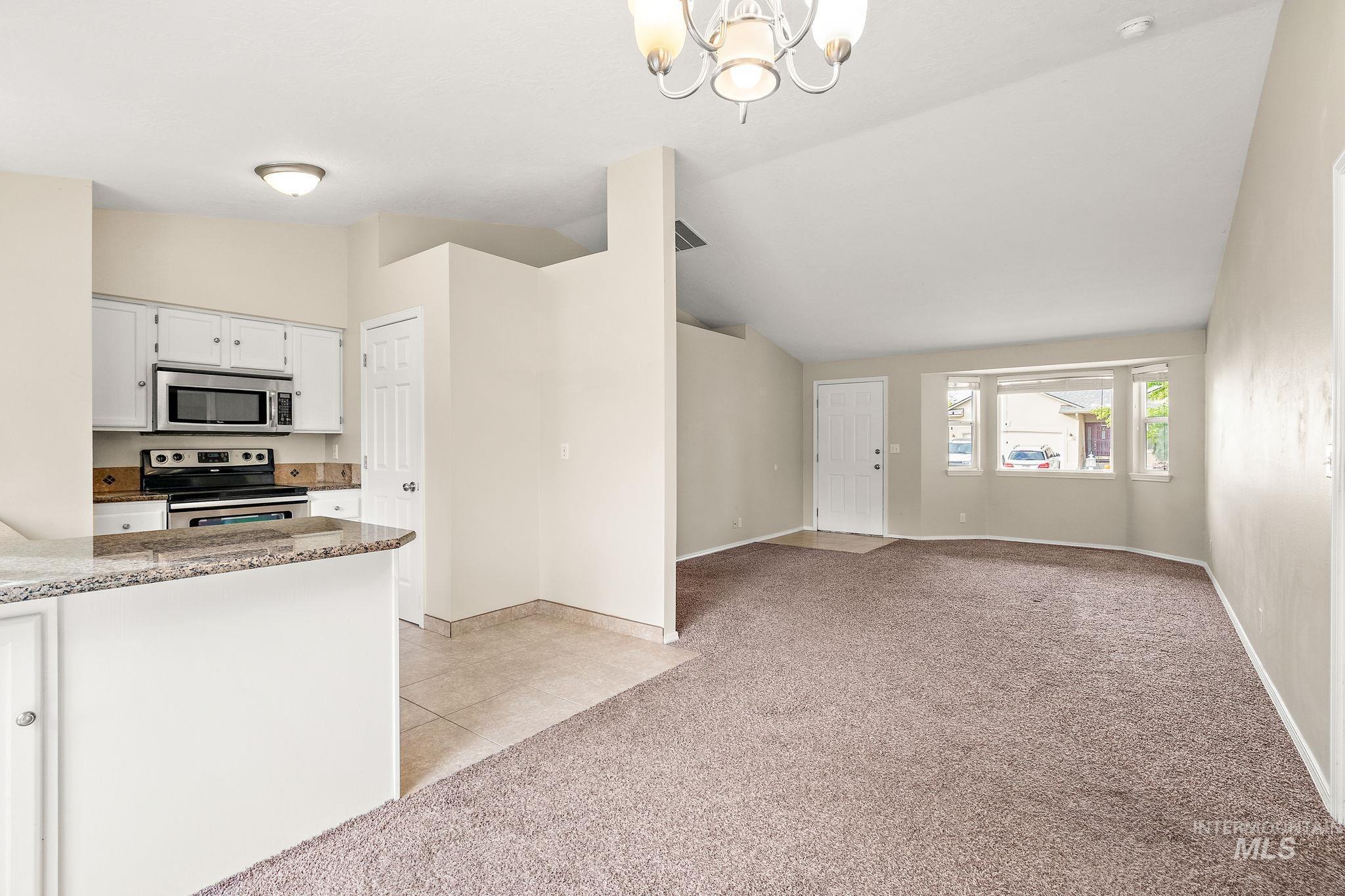 Kitchen with vaulted ceiling, white cabinets, light carpet, light stone countertops, and a chandelier
