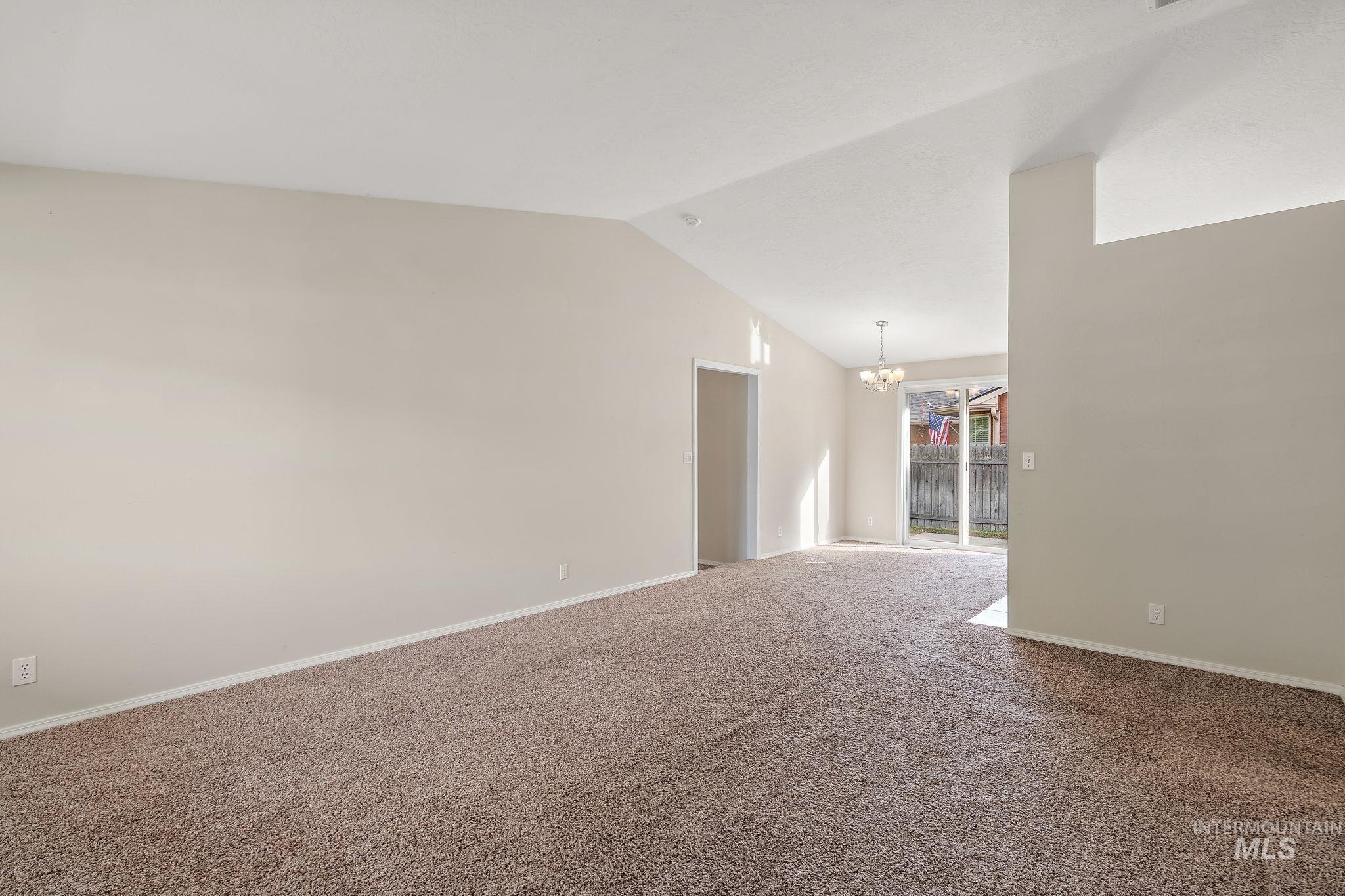 Carpeted empty room with a chandelier and lofted ceiling