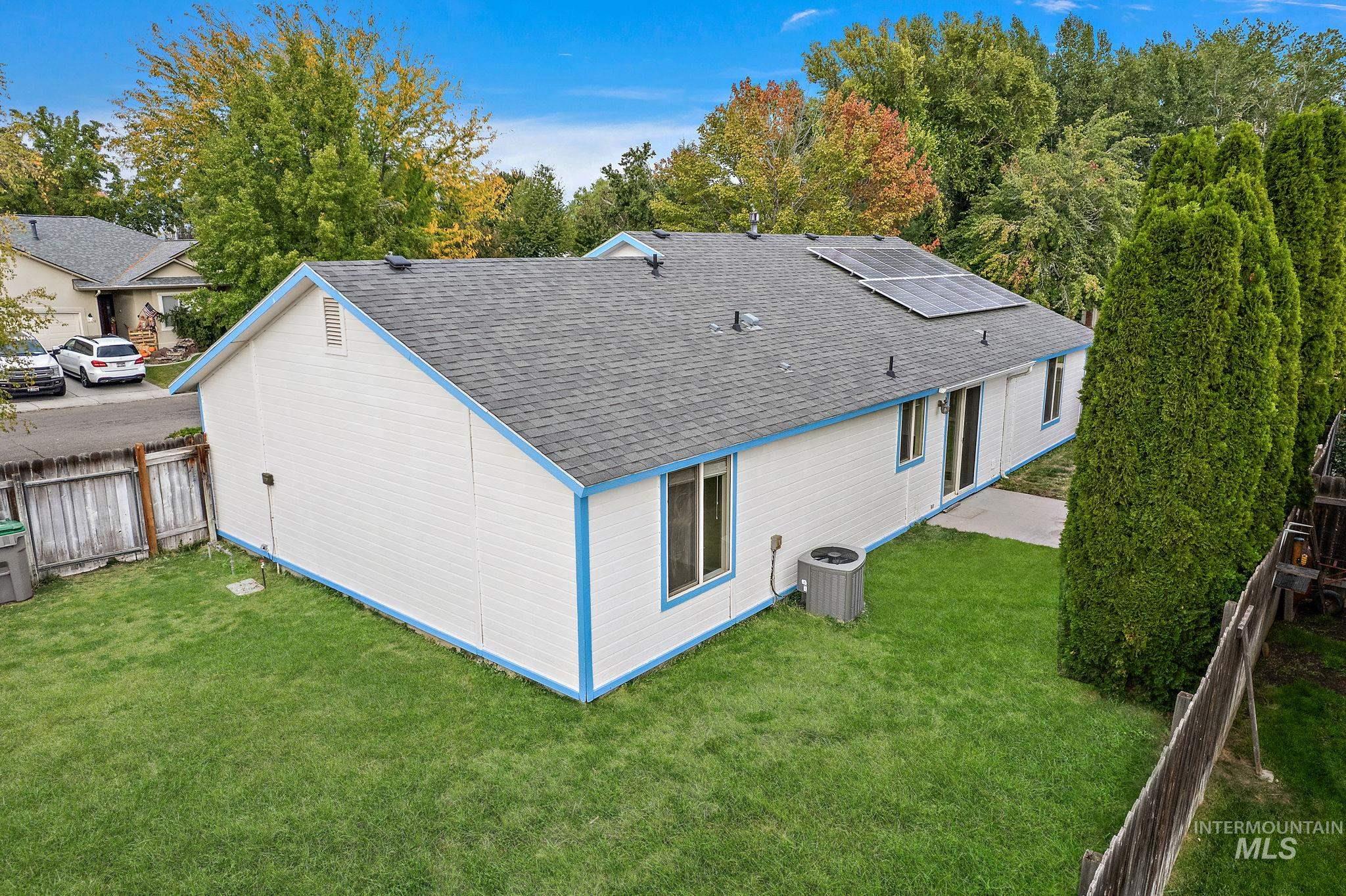Back of house featuring roof with shingles, solar panels, and a fenced backyard