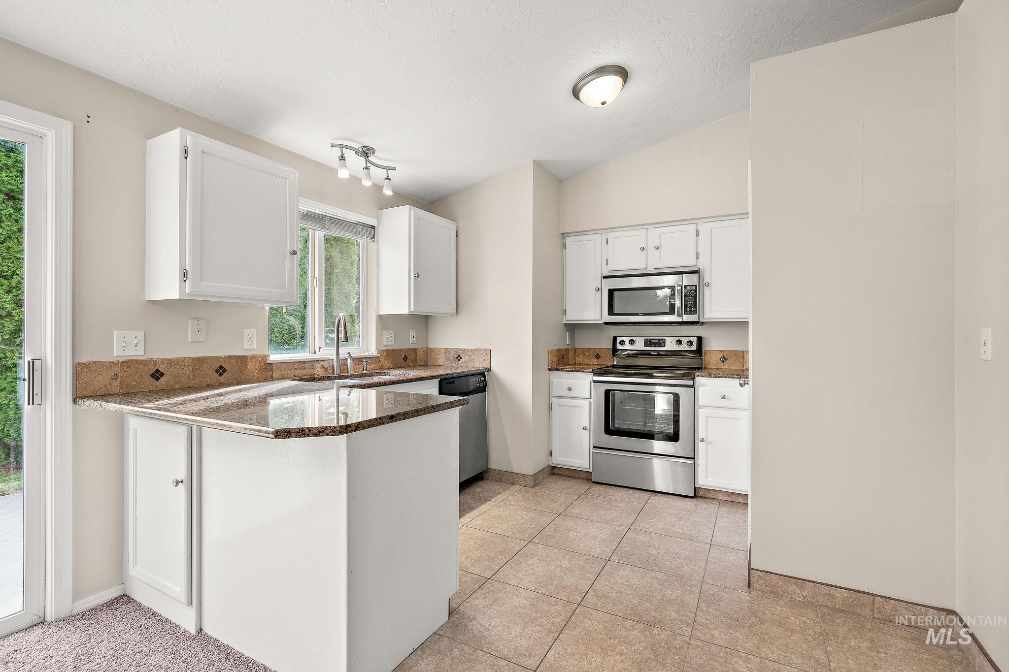 Kitchen with appliances with stainless steel finishes, white cabinetry, a peninsula, dark stone counters, and vaulted ceiling