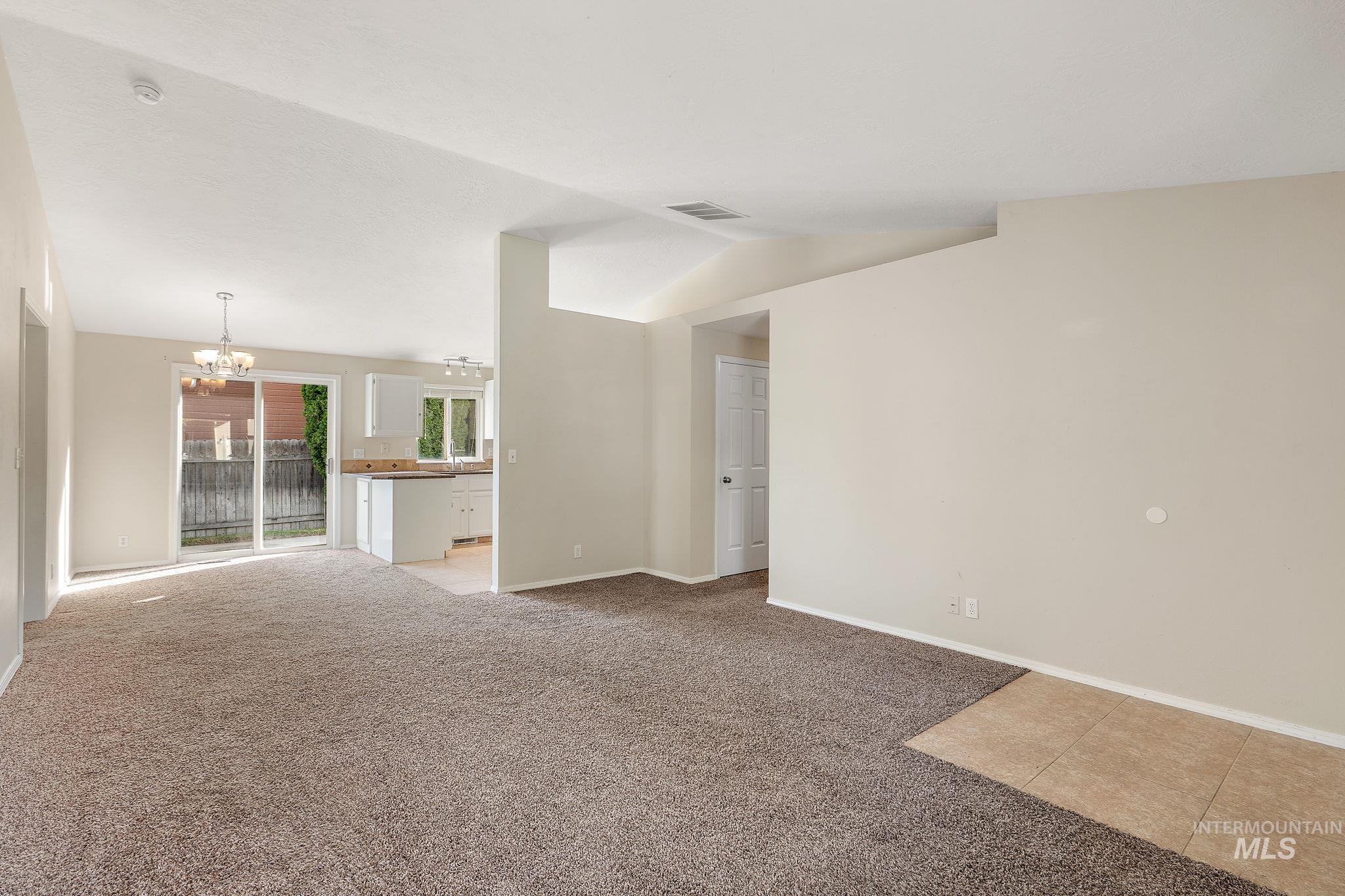 Spare room featuring light colored carpet, a chandelier, and vaulted ceiling