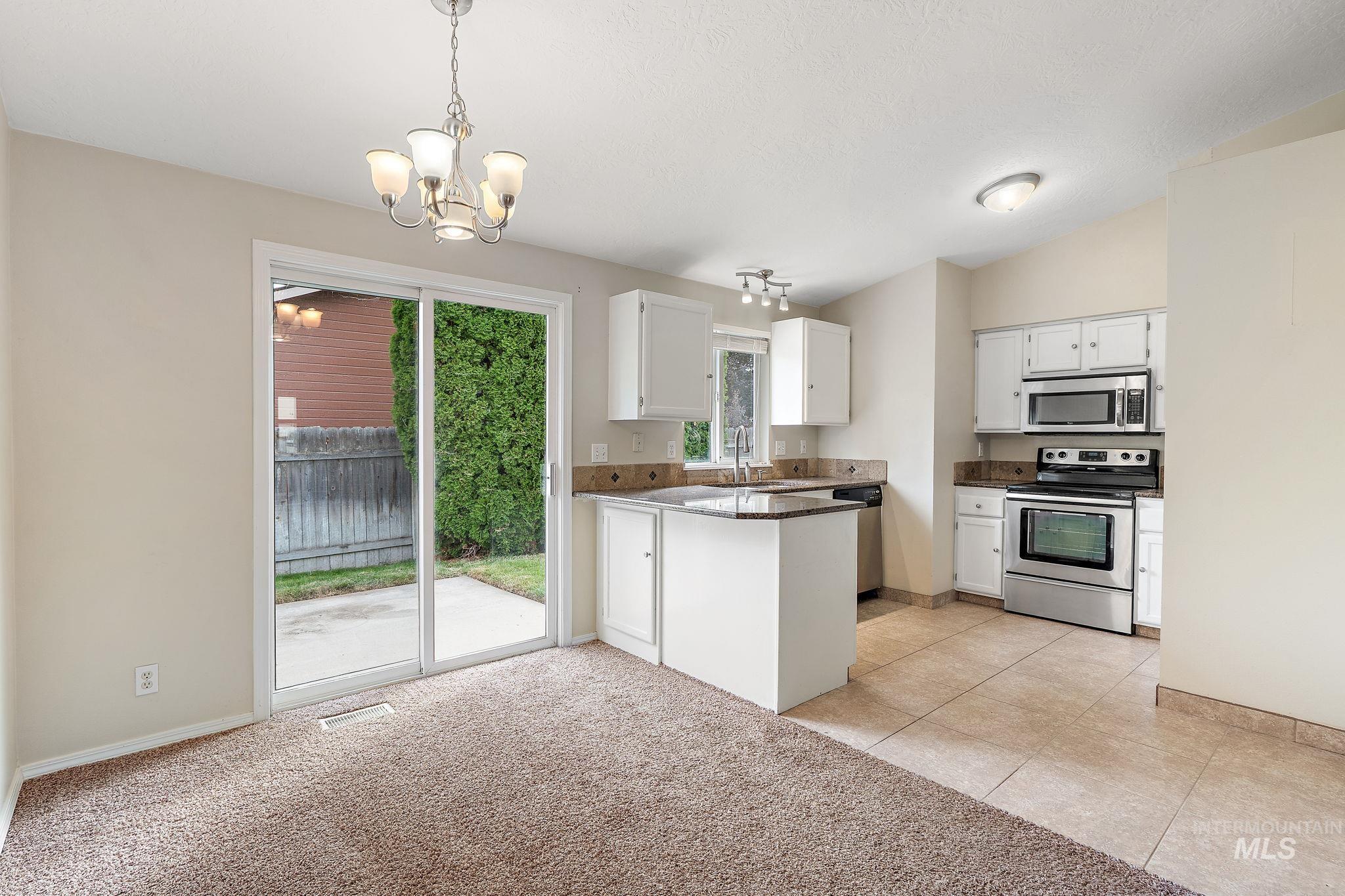Kitchen with appliances with stainless steel finishes, light colored carpet, hanging light fixtures, light tile patterned floors, and white cabinets