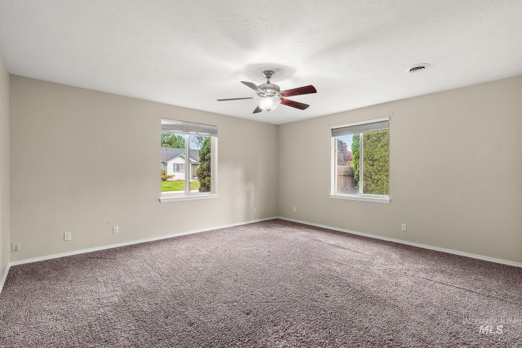 Unfurnished room with healthy amount of natural light, carpet flooring, a ceiling fan, and a textured ceiling
