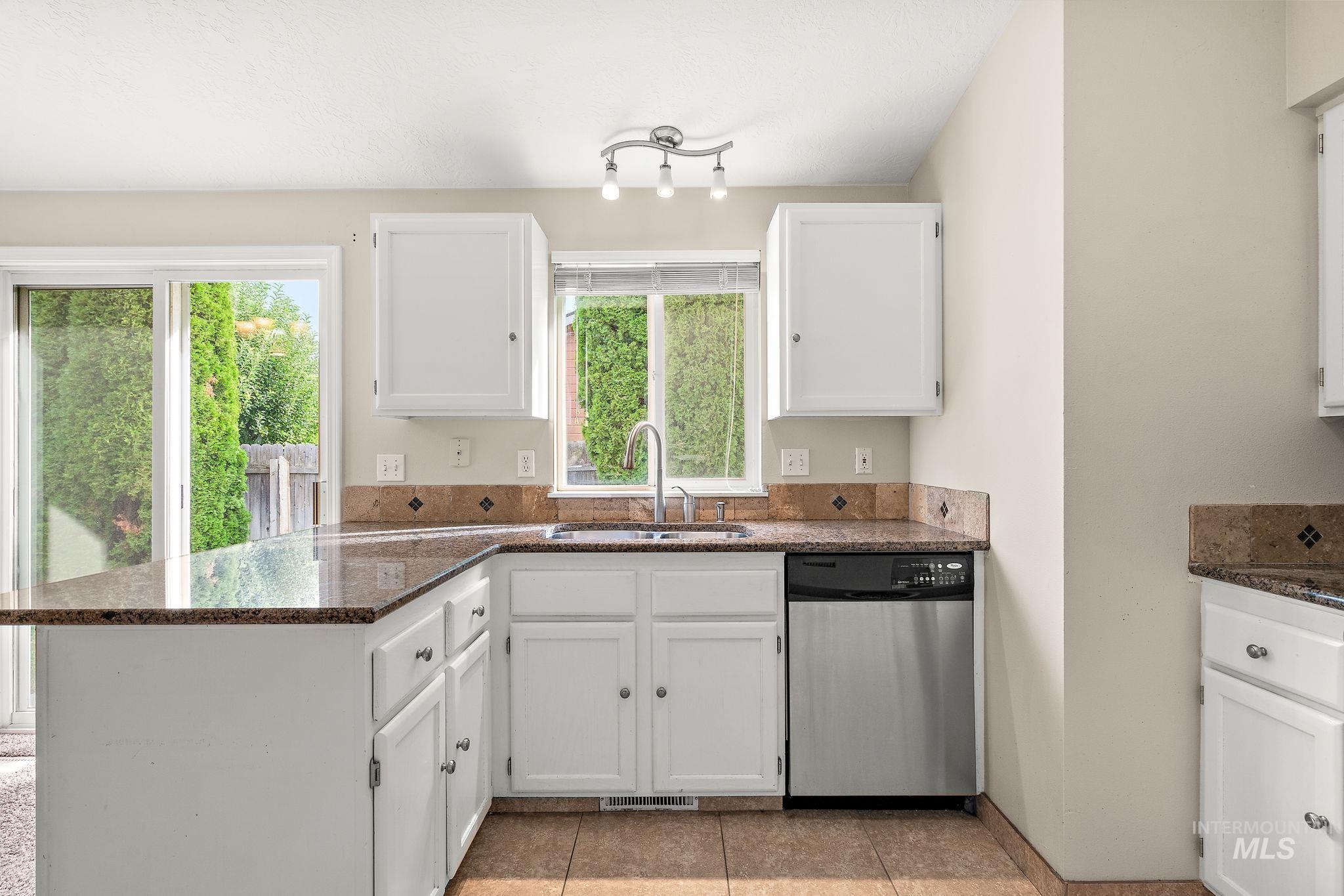 Kitchen featuring a peninsula, stainless steel dishwasher, white cabinets, dark stone counters, and light tile patterned floors