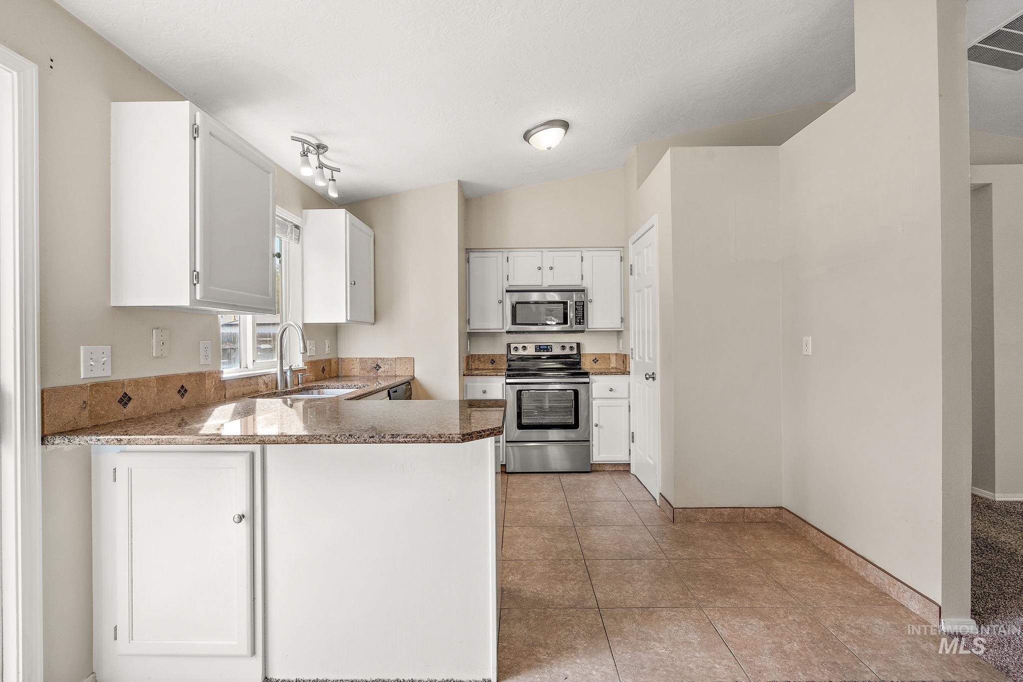 Kitchen with appliances with stainless steel finishes, white cabinets, a peninsula, light tile patterned flooring, and light stone counters