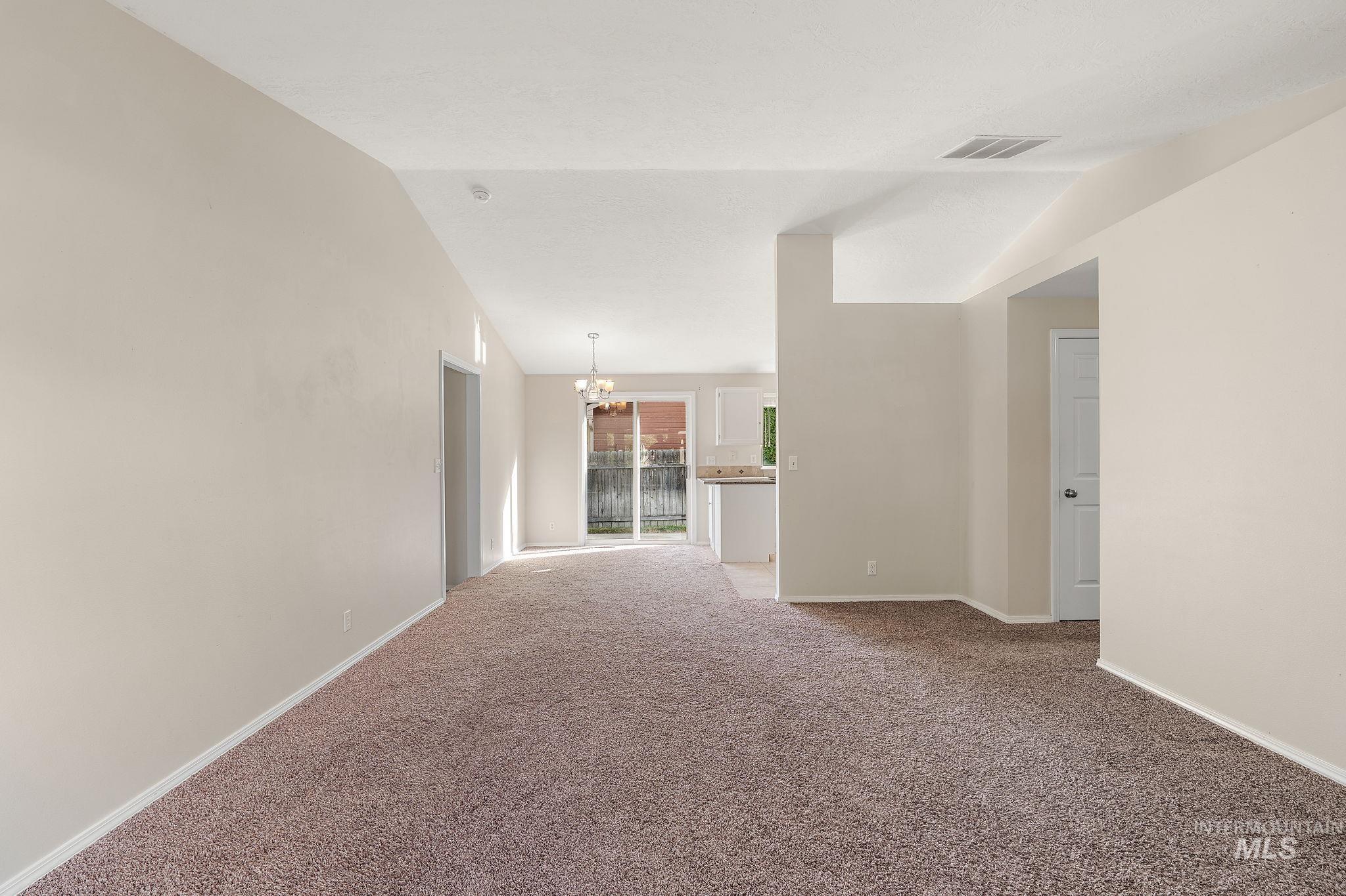 Carpeted empty room with a chandelier and vaulted ceiling