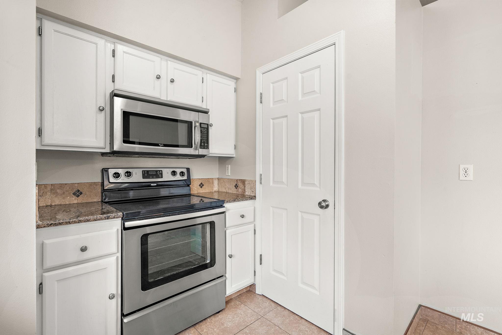 Kitchen featuring stainless steel appliances, white cabinets, dark stone counters, and light tile patterned floors