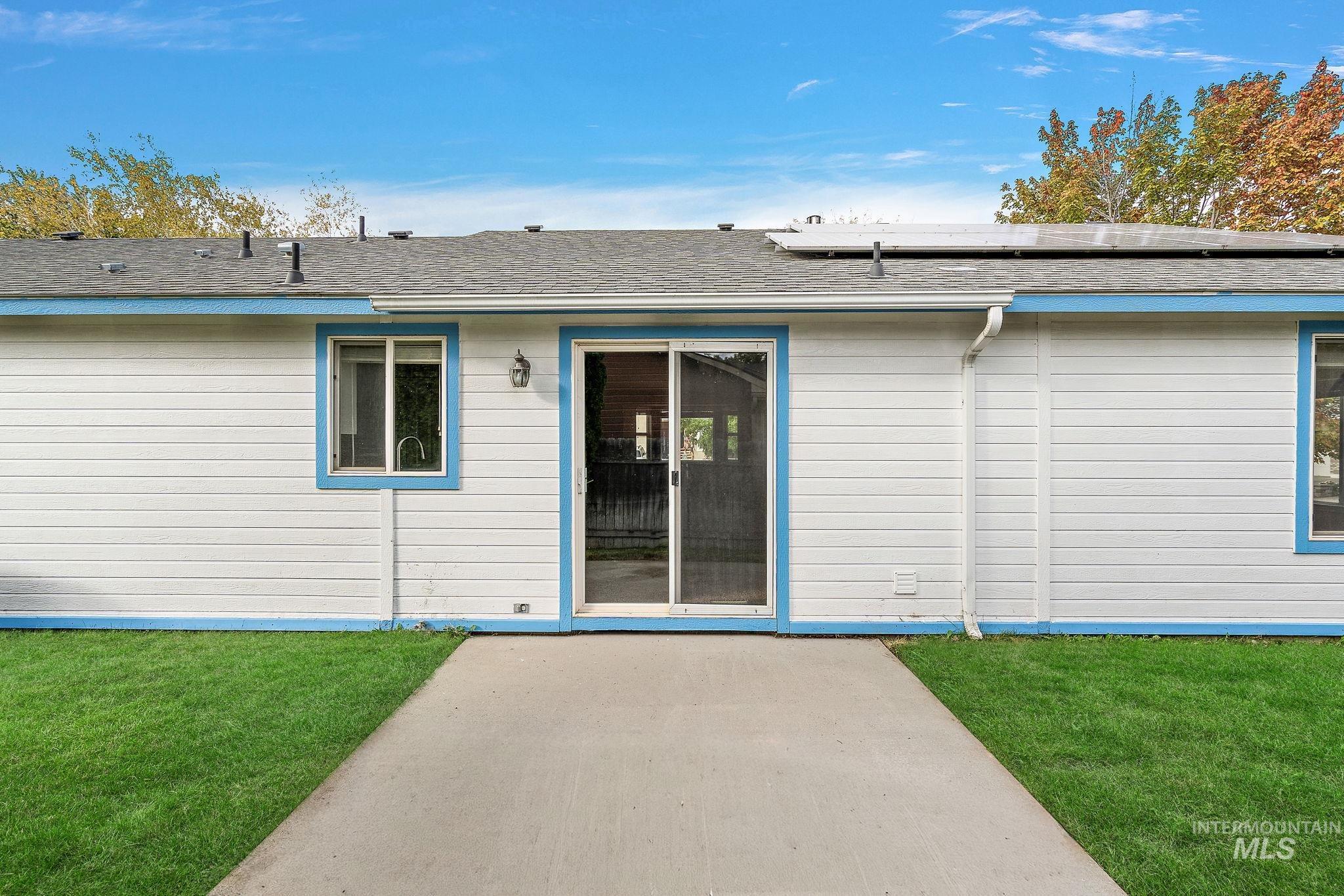 Rear view of house with roof with shingles, a yard, and roof mounted solar panels