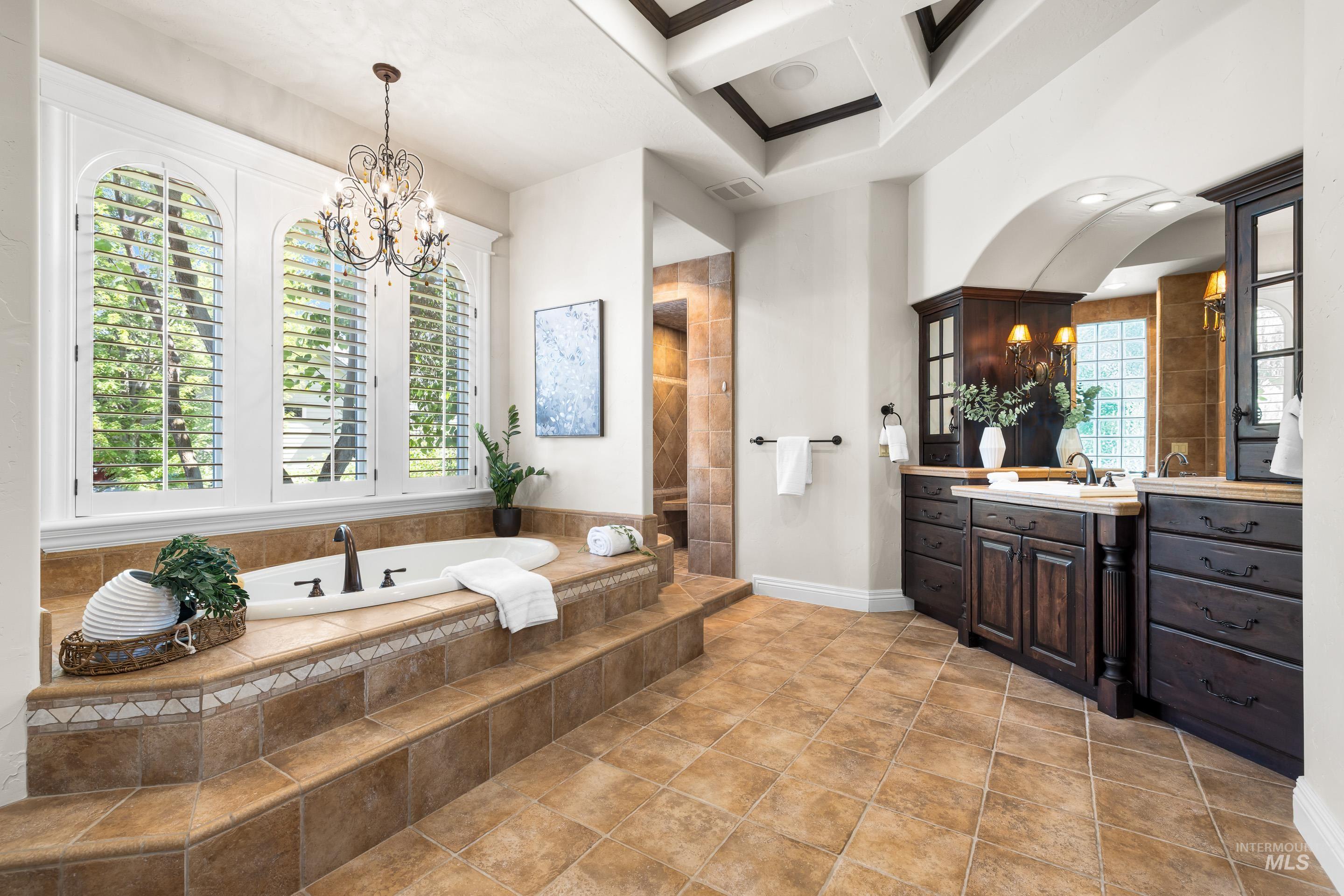 Bathroom featuring vanity, a bath, a chandelier, and tiled shower