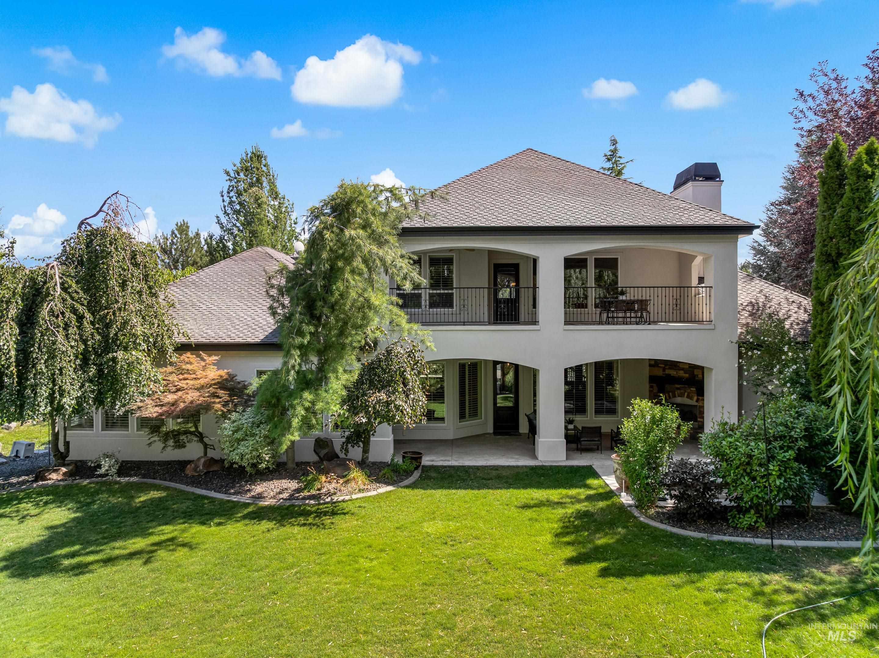 Rear view of house with stucco siding, a chimney, a patio, a lawn, and a shingled roof
